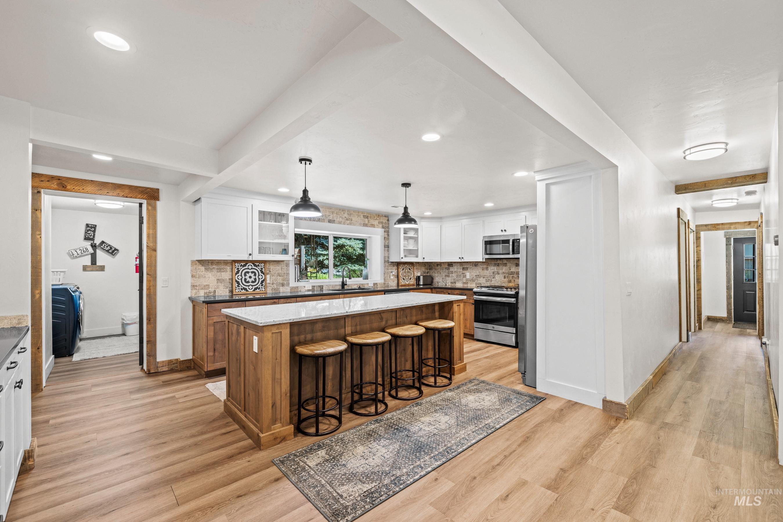 Kitchen with appliances with stainless steel finishes, light wood-style flooring, a breakfast bar, backsplash, and recessed lighting