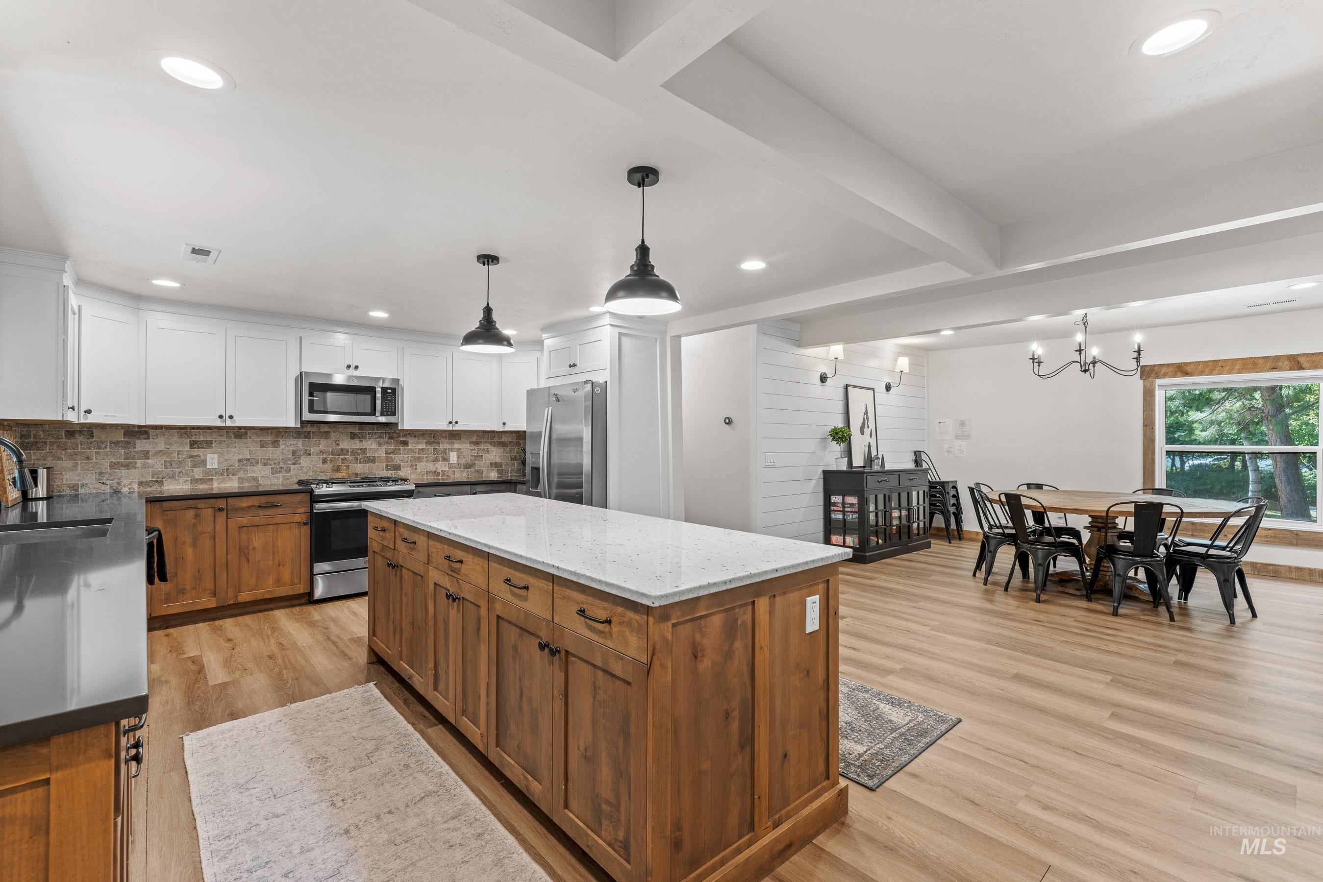 Kitchen featuring appliances with stainless steel finishes, light wood-type flooring, decorative backsplash, white cabinetry, and a center island