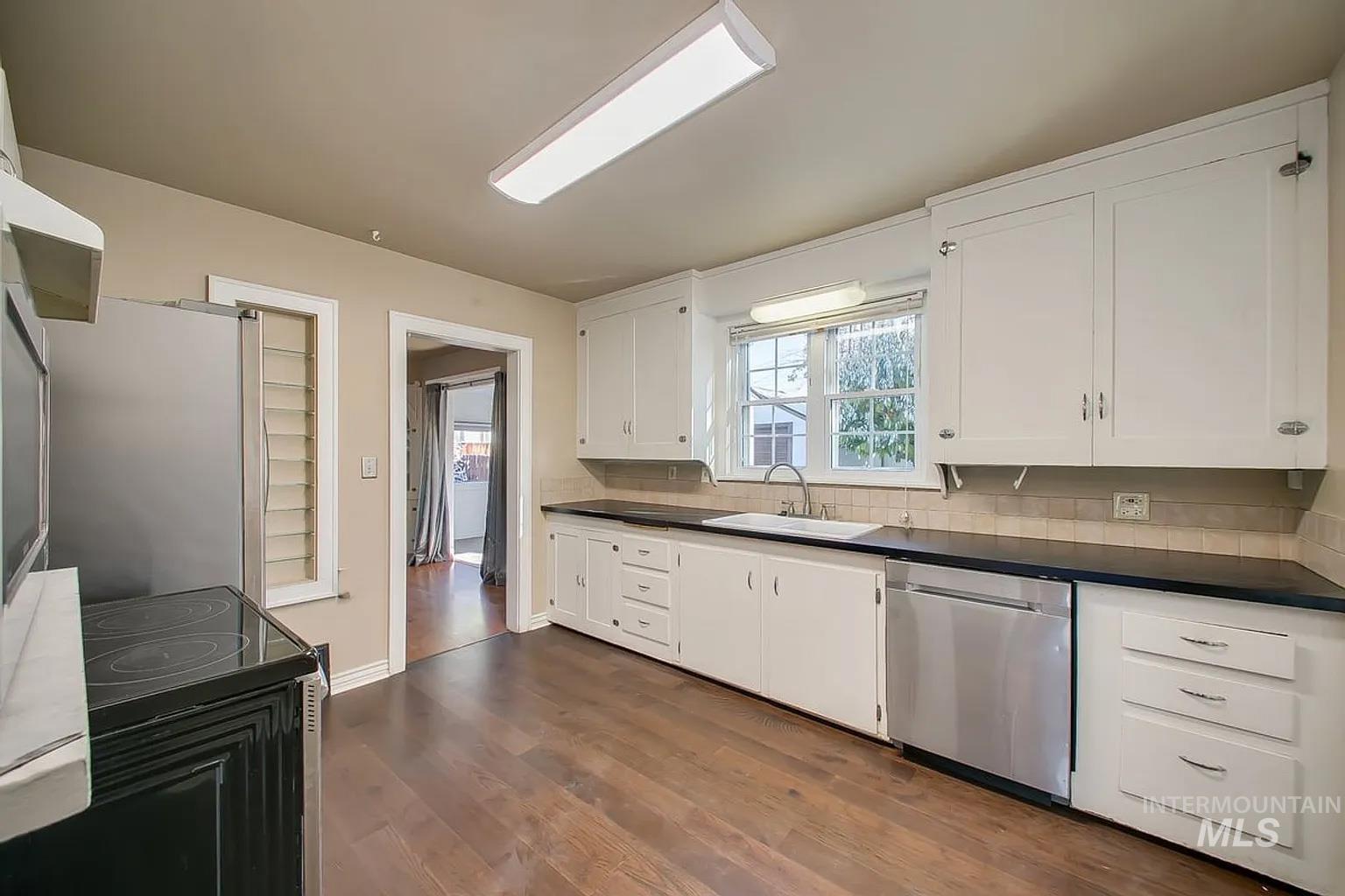 Kitchen with stainless steel appliances, dark countertops, backsplash, and white cabinets