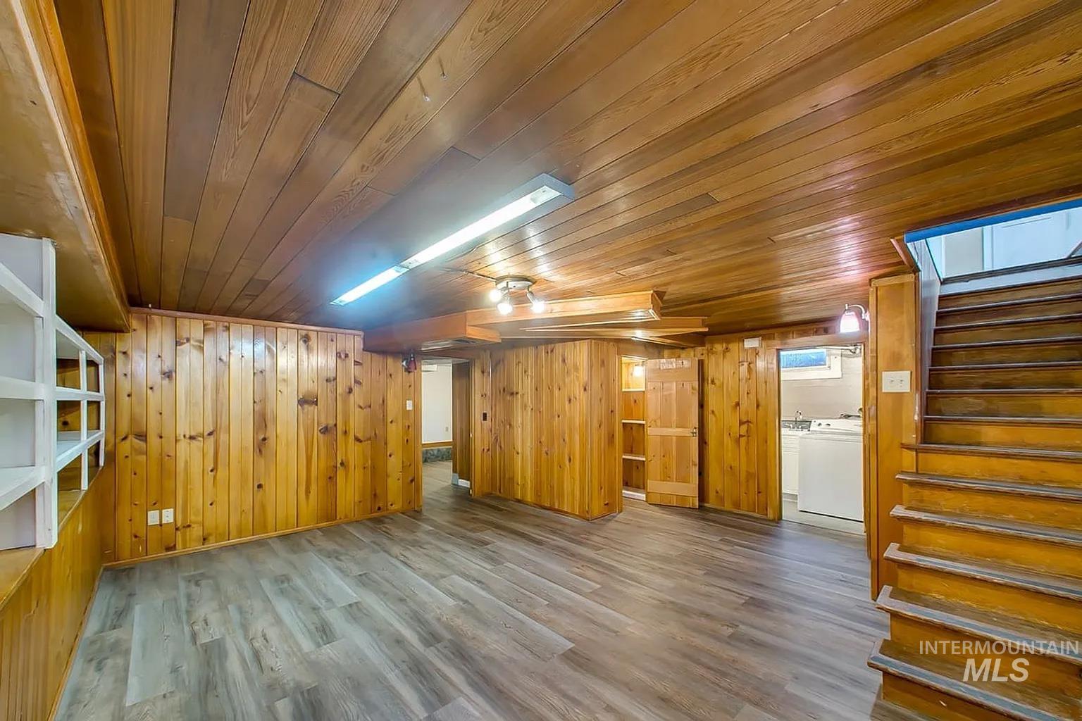 Below grade area with wooden ceiling, stairway, washer and clothes dryer, wood finished floors, and wooden walls
