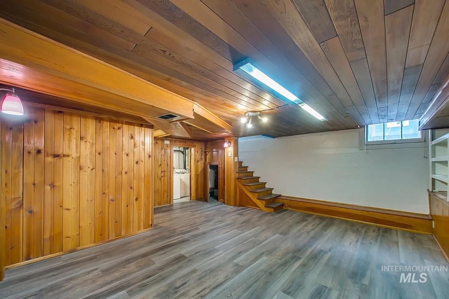 Basement with washer / clothes dryer, wooden ceiling, stairway, wood finished floors, and wooden walls