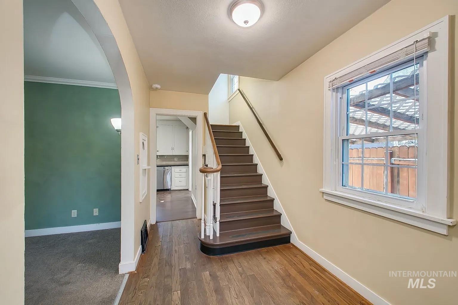 Staircase featuring arched walkways, wood finished floors, and ornamental molding