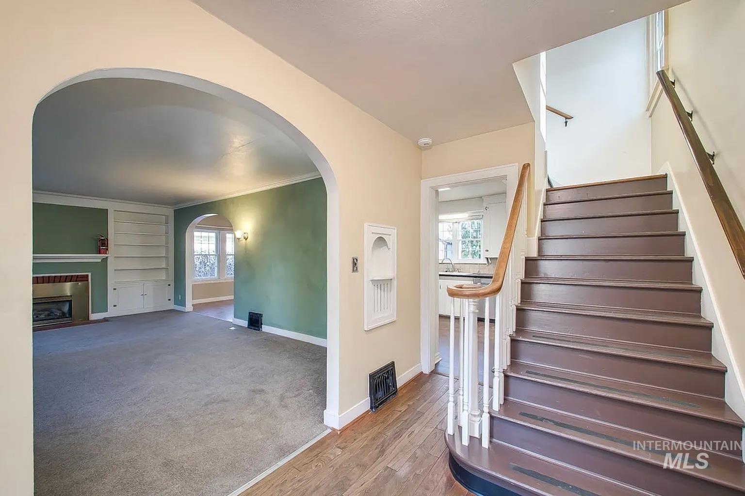 Stairs with arched walkways, a fireplace, and wood finished floors