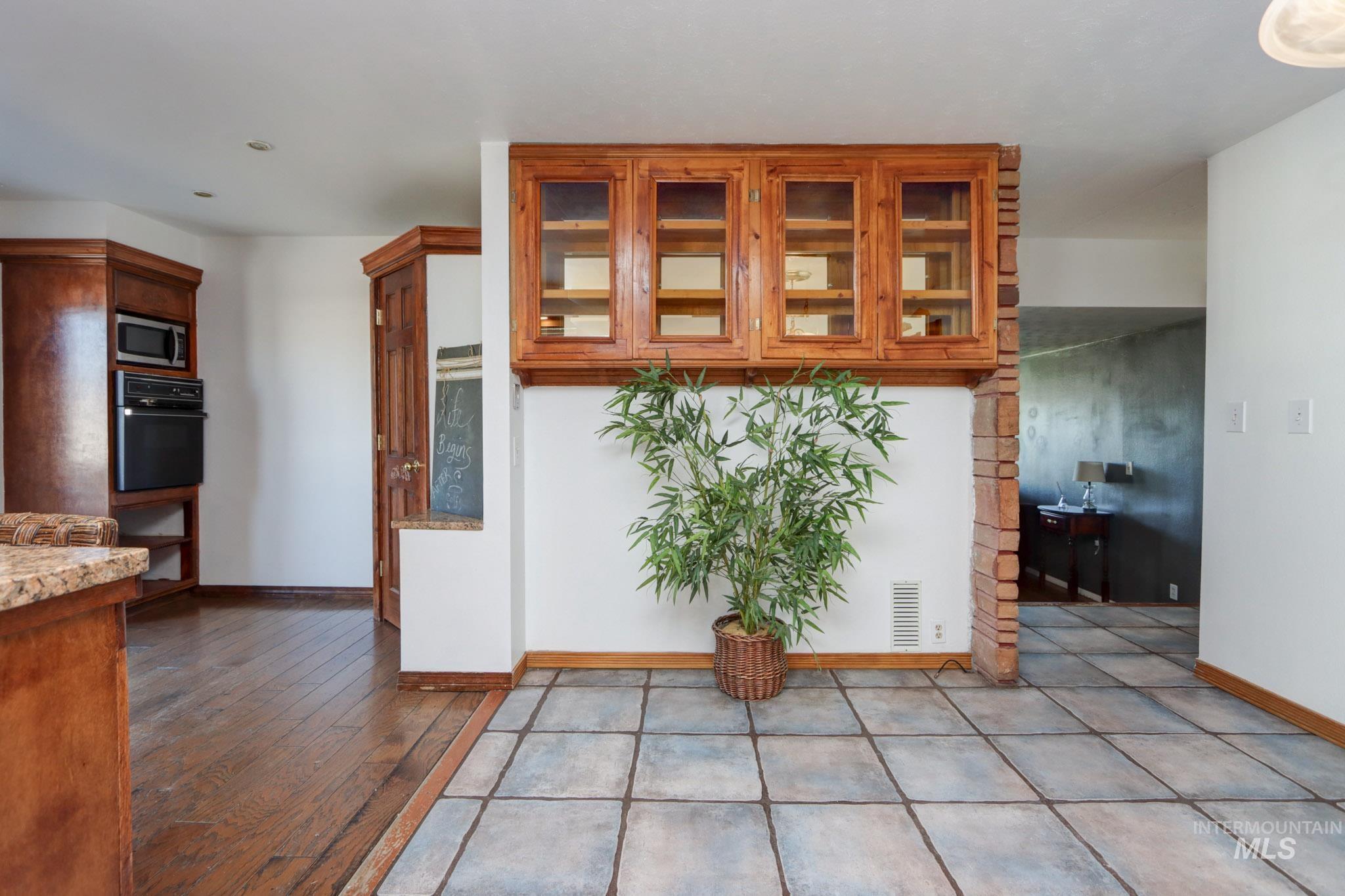 Kitchen featuring oven, stainless steel microwave, brown cabinetry, glass insert cabinets, and light stone counters
