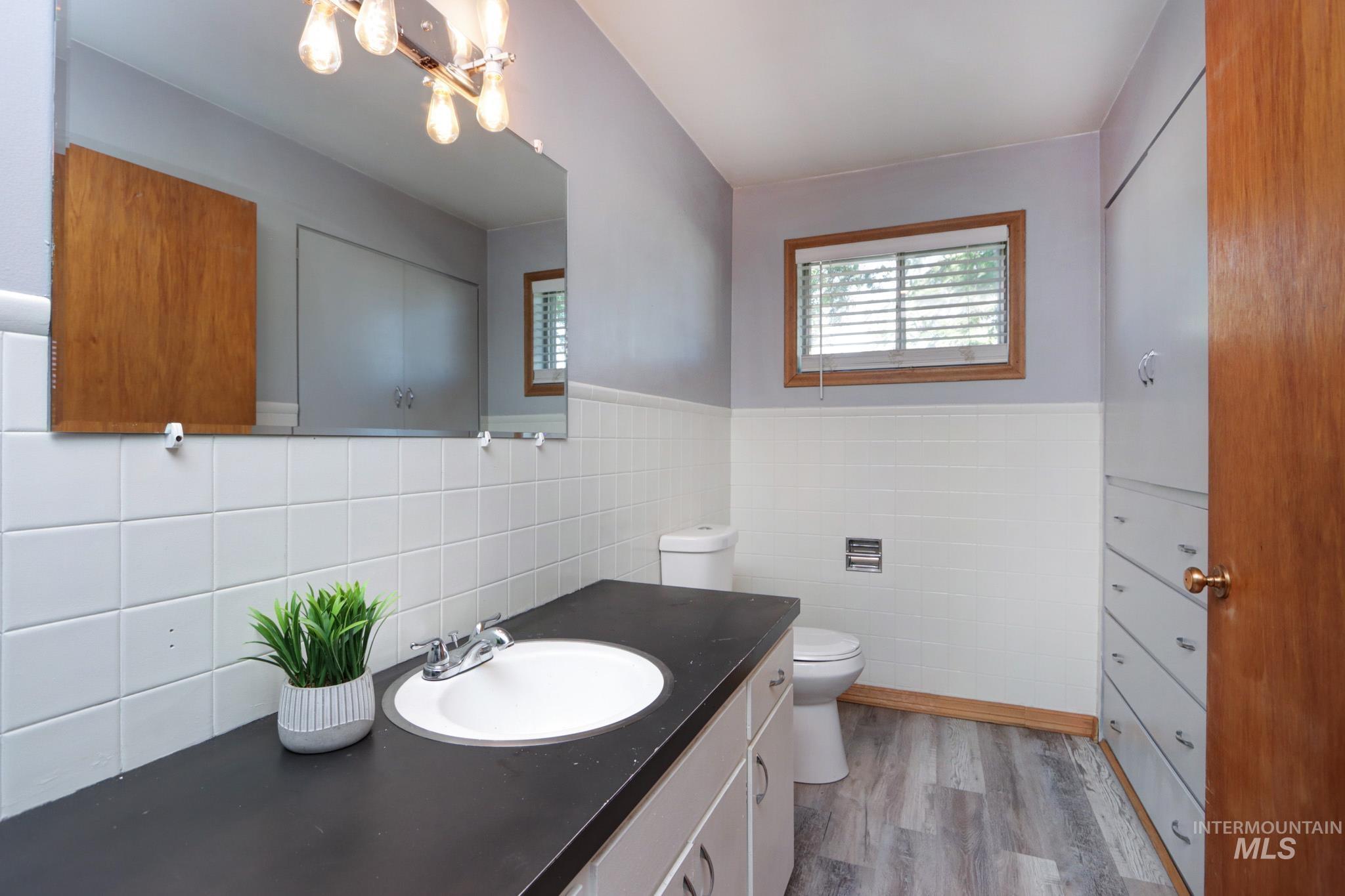 Bathroom with tile walls, wood finished floors, vanity, a chandelier, and a wainscoted wall