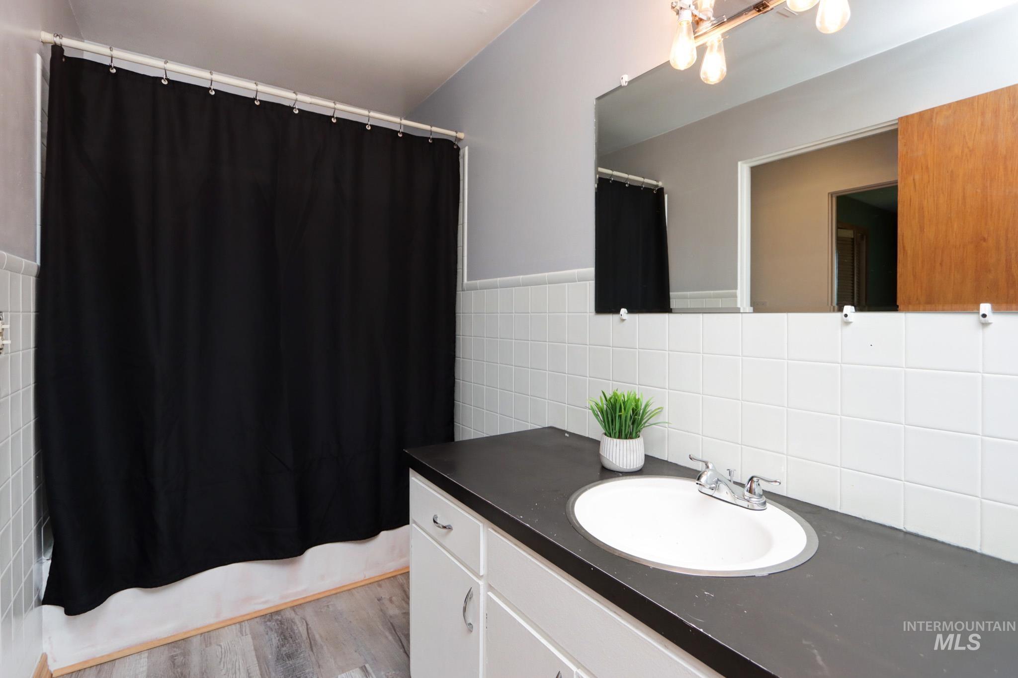 Bathroom featuring vanity, tile walls, shower / tub combo, and wood finished floors