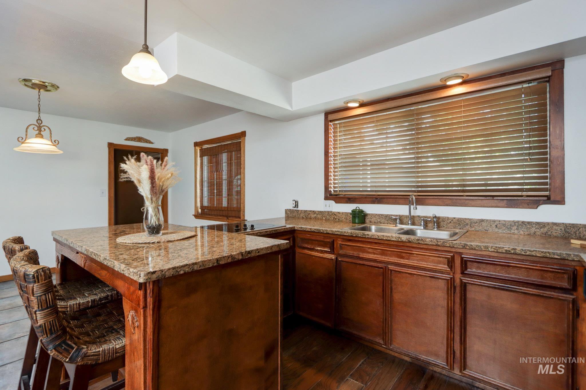 Kitchen with dark wood-type flooring, hanging light fixtures, a kitchen island, light stone counters, and a breakfast bar