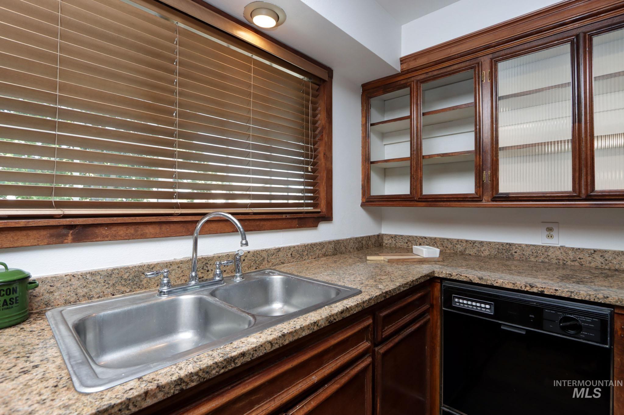 Kitchen featuring black dishwasher, glass insert cabinets, light countertops, and dark brown cabinets