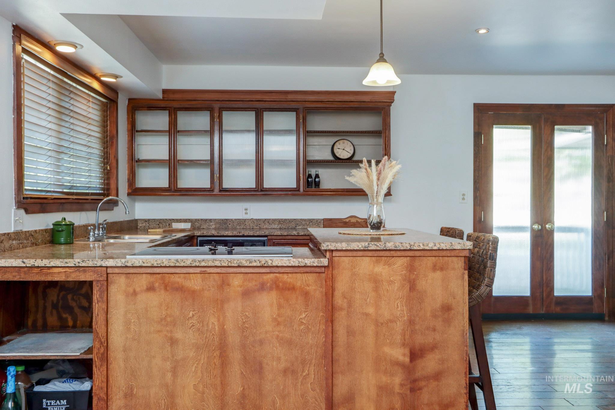 Kitchen featuring glass insert cabinets, wood-type flooring, pendant lighting, a peninsula, and recessed lighting