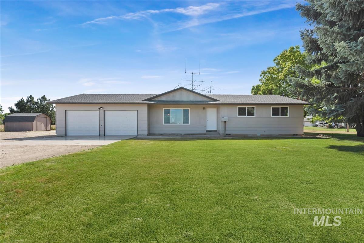 Ranch-style house featuring dirt driveway, a shed, an attached garage, and a front lawn