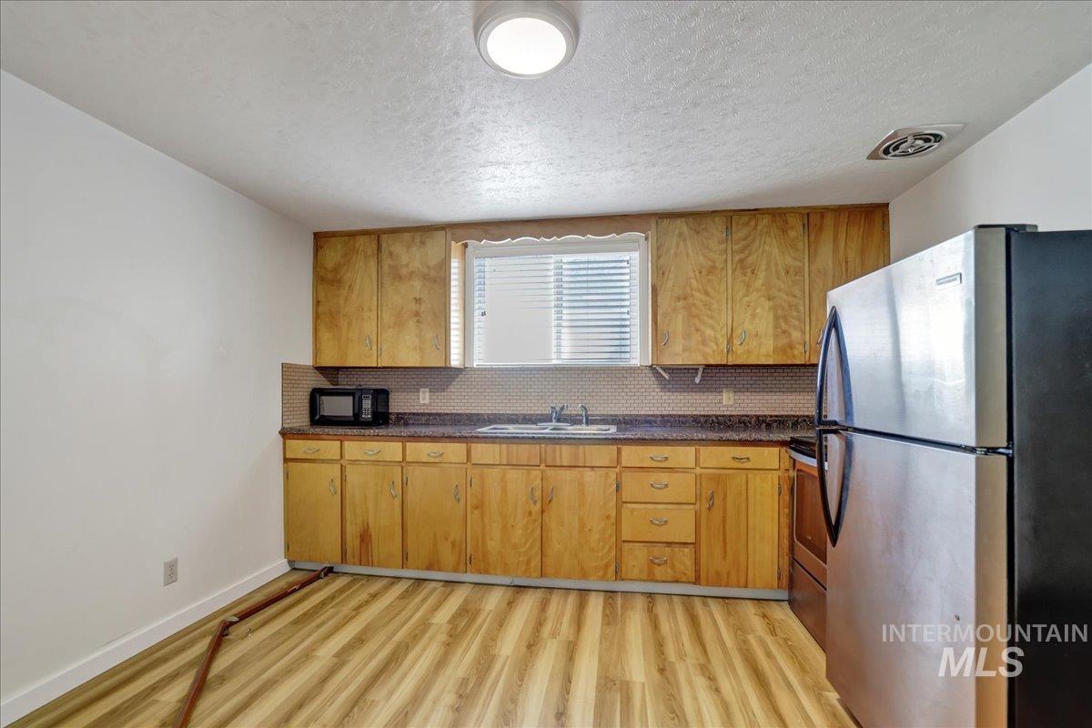 Kitchen with stainless steel appliances, dark countertops, light wood-style flooring, and a textured ceiling
