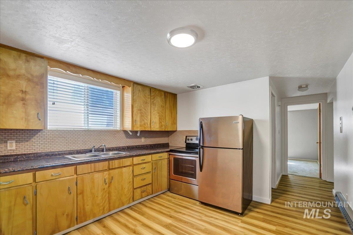 Kitchen with appliances with stainless steel finishes, light wood-type flooring, a textured ceiling, backsplash, and dark countertops