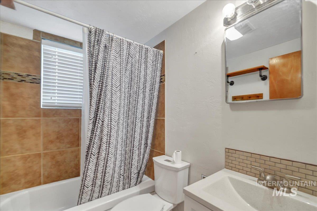 Full bath featuring shower / bath combo with shower curtain, backsplash, and vanity