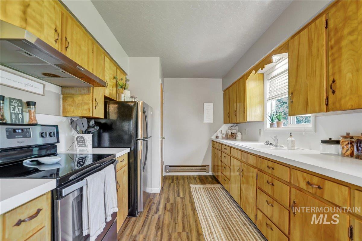 Kitchen featuring stainless steel electric range, under cabinet range hood, wood finished floors, light countertops, and baseboard heating