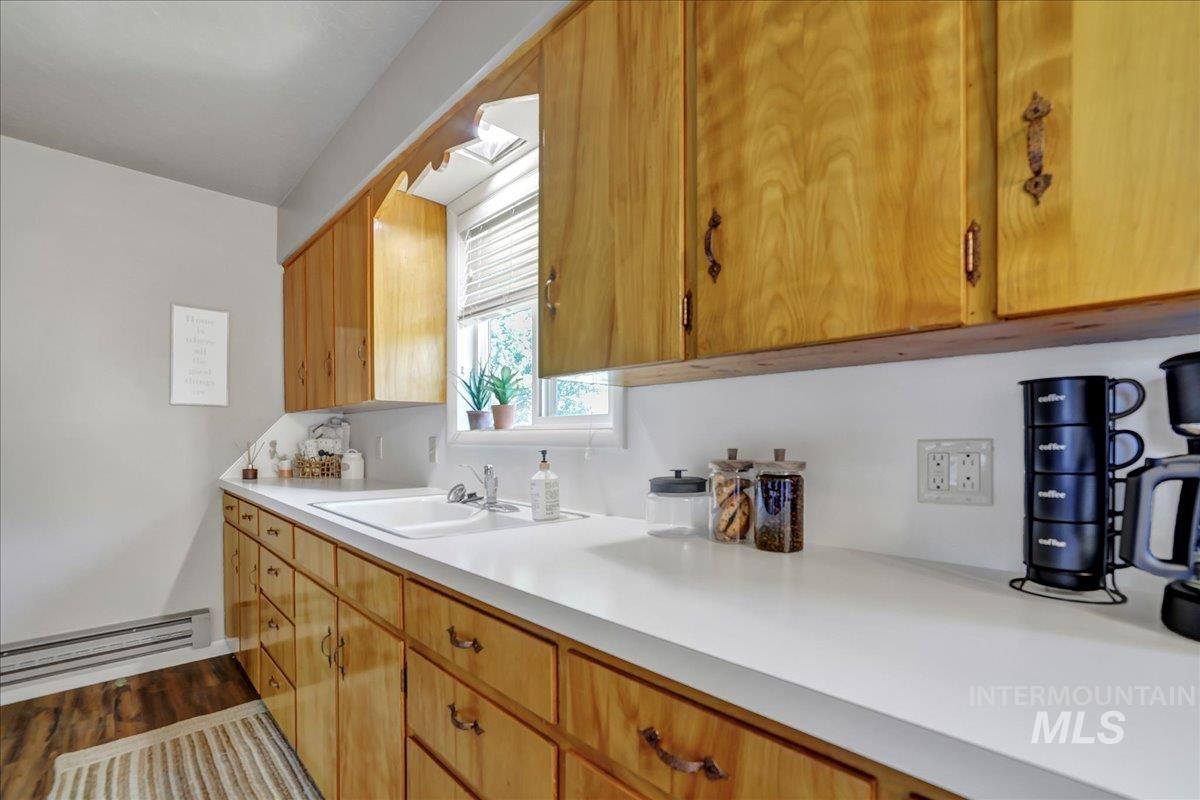 Kitchen featuring light countertops, a baseboard heating unit, wood finished floors, and brown cabinetry