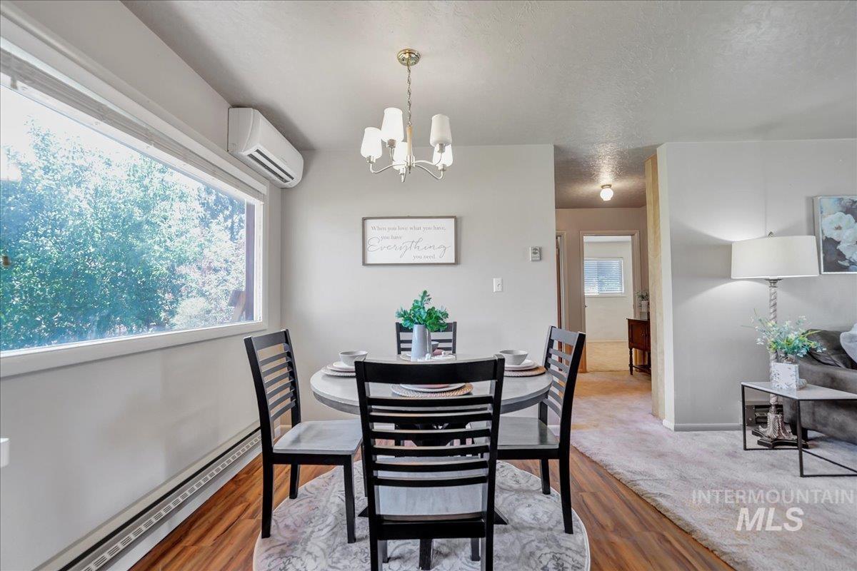 Dining space featuring a wall mounted air conditioner, a chandelier, a baseboard radiator, wood finished floors, and a textured ceiling
