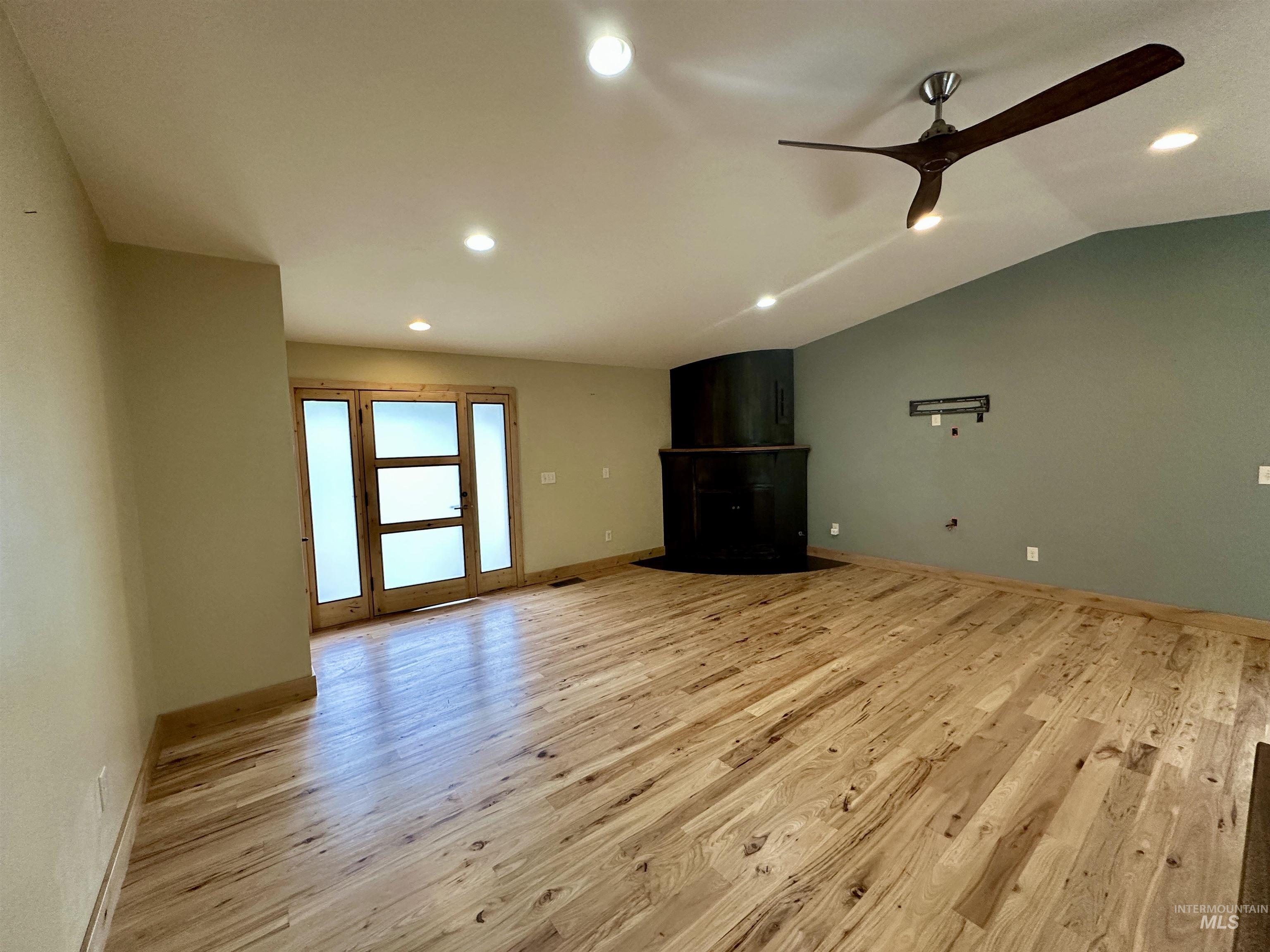 Unfurnished living room with light wood-type flooring, a ceiling fan, recessed lighting, a fireplace with flush hearth, and vaulted ceiling