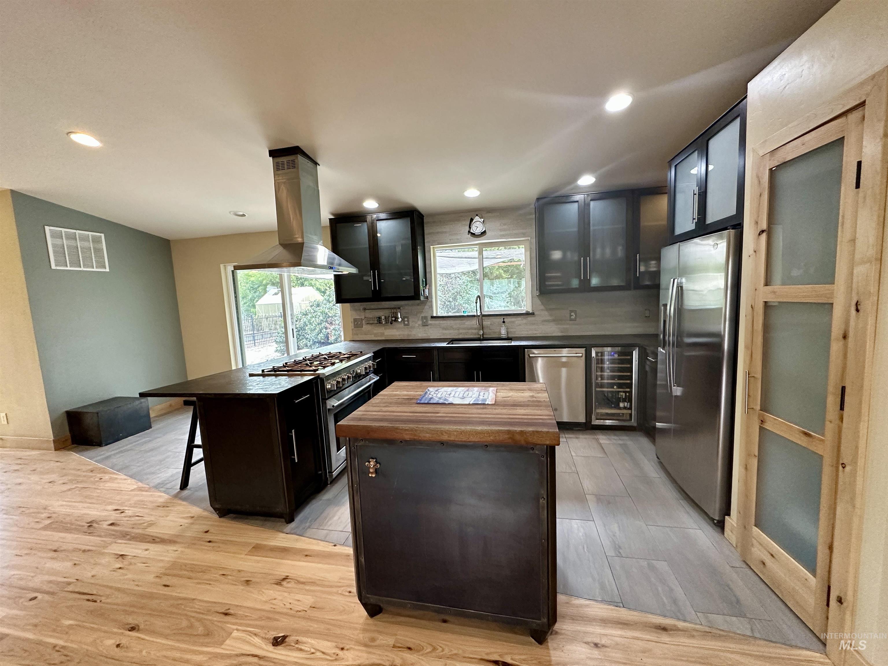 Kitchen with stainless steel appliances, island exhaust hood, a center island, light wood-type flooring, and a breakfast bar area