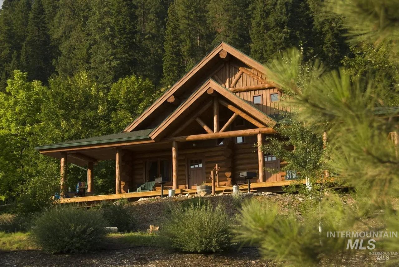 View of front of large twin cabin featuring log siding, a porch, and a view of trees