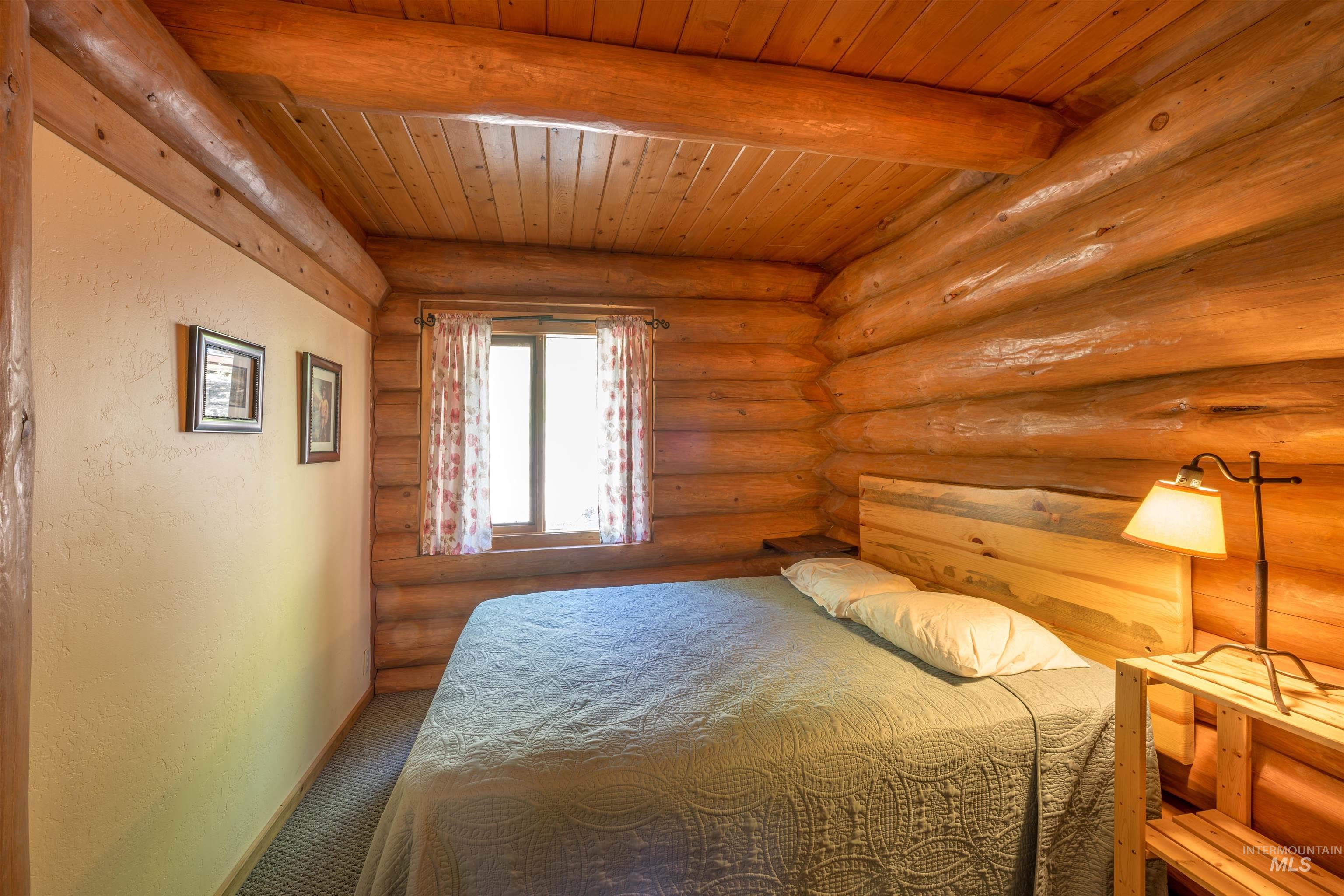 Carpeted bedroom featuring a wooden ceiling with exposed beams and log walls
