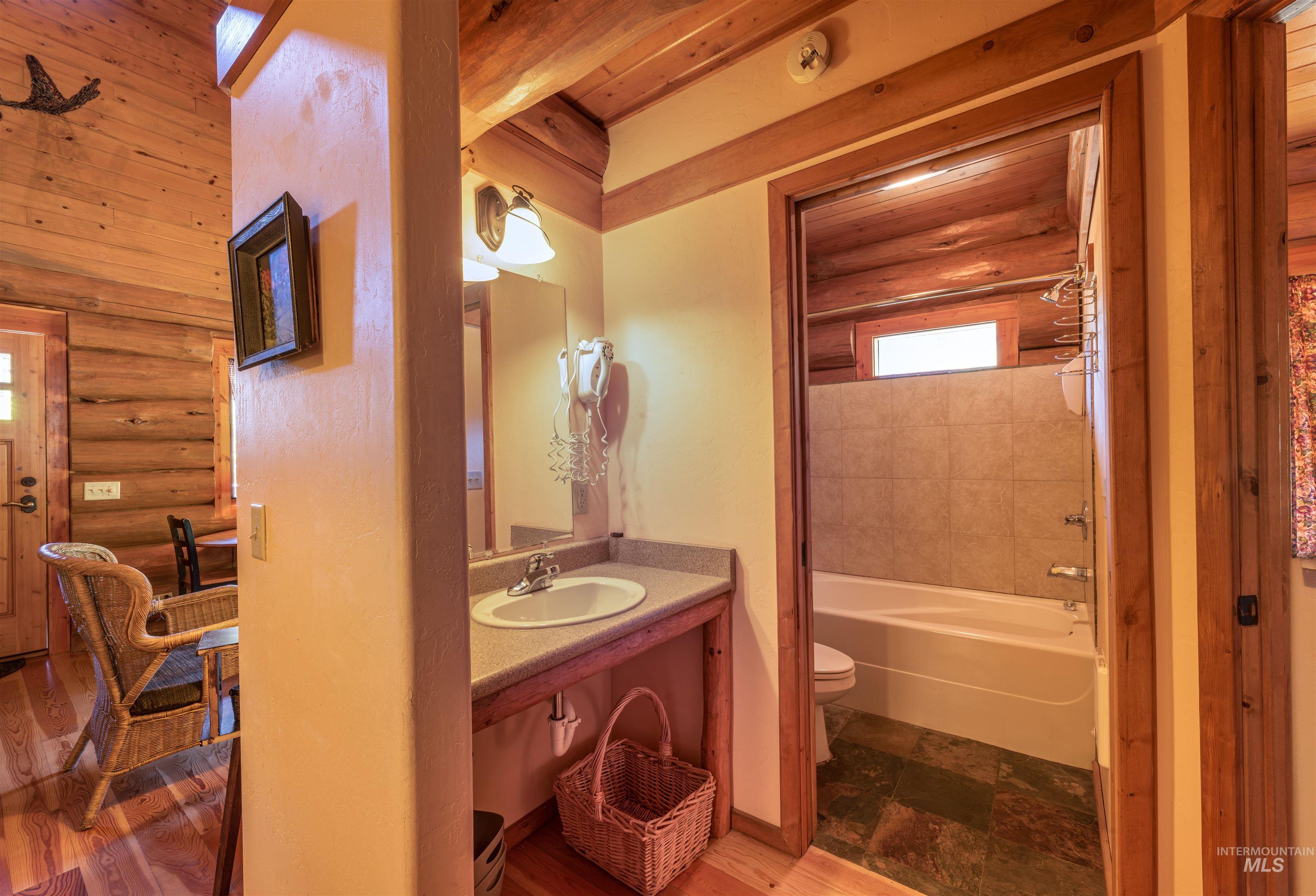 Full bathroom featuring log walls, vanity, washtub / shower combination, and wood finished floors