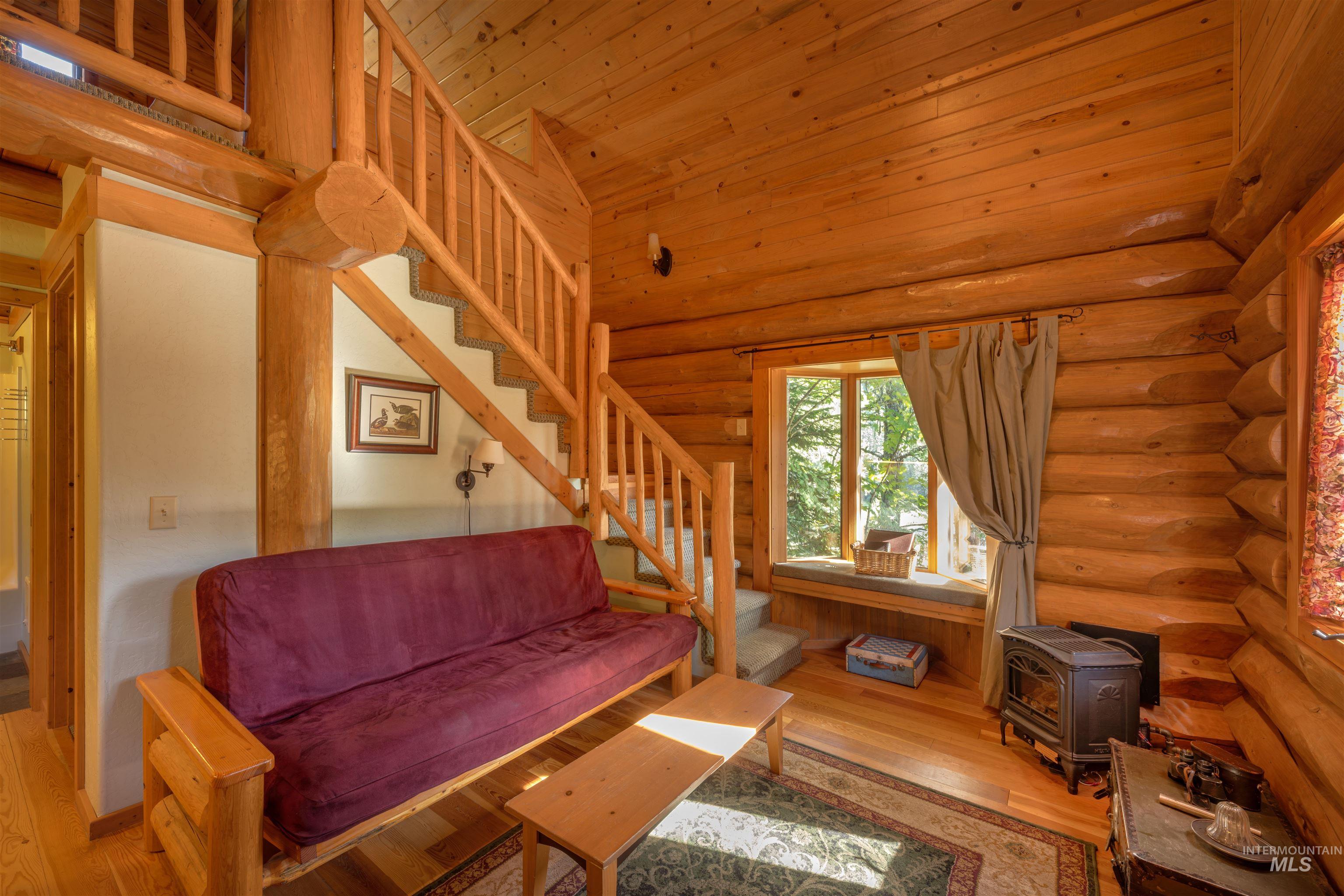 Living room featuring a wood stove, stairway, rustic walls, and wood finished floors
