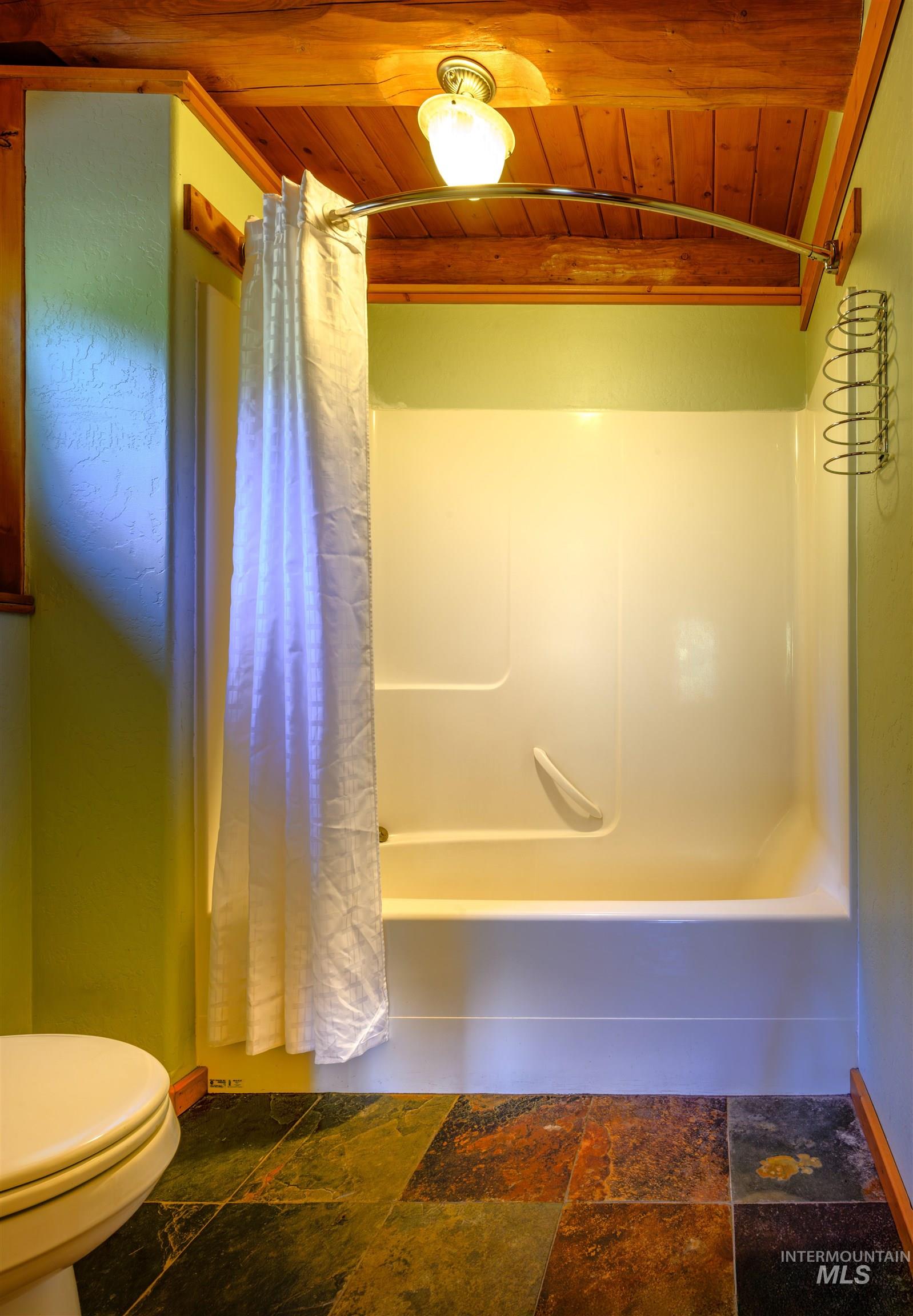 Full bathroom with wooden ceiling, shower / tub combo, and stone tile flooring