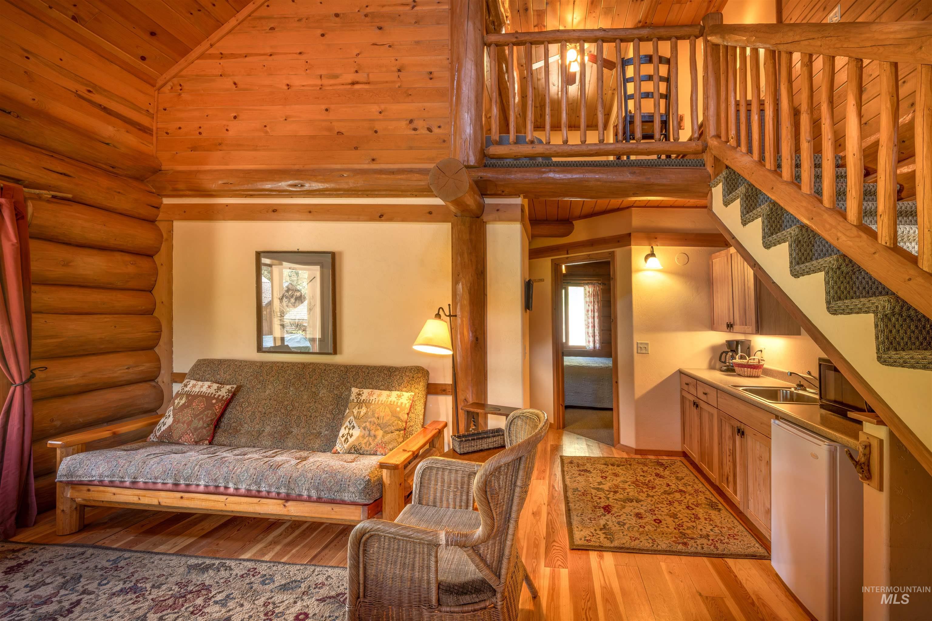 Living room with high vaulted ceiling, log walls, light wood-type flooring, stairway, and wood ceiling