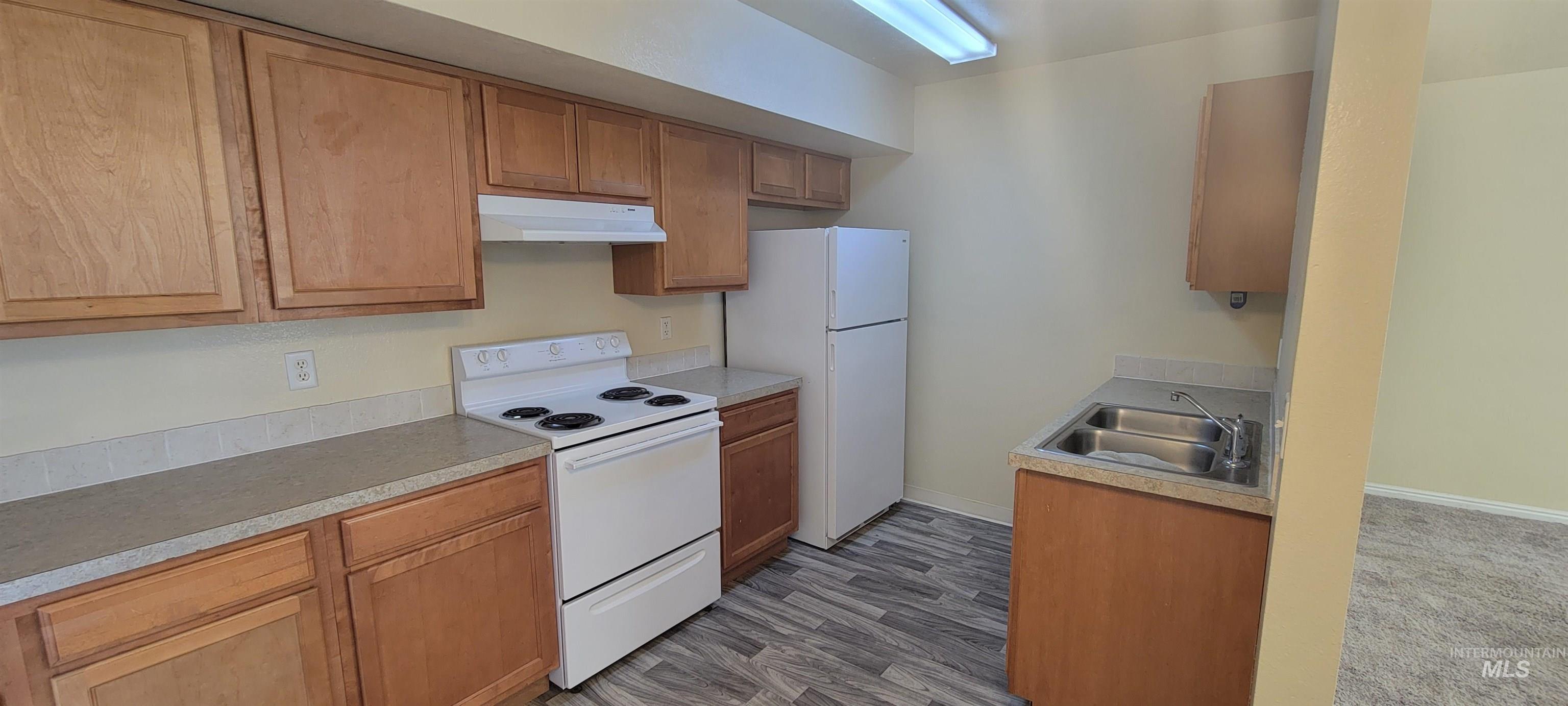 Kitchen with white appliances, under cabinet range hood, light countertops, and brown cabinets