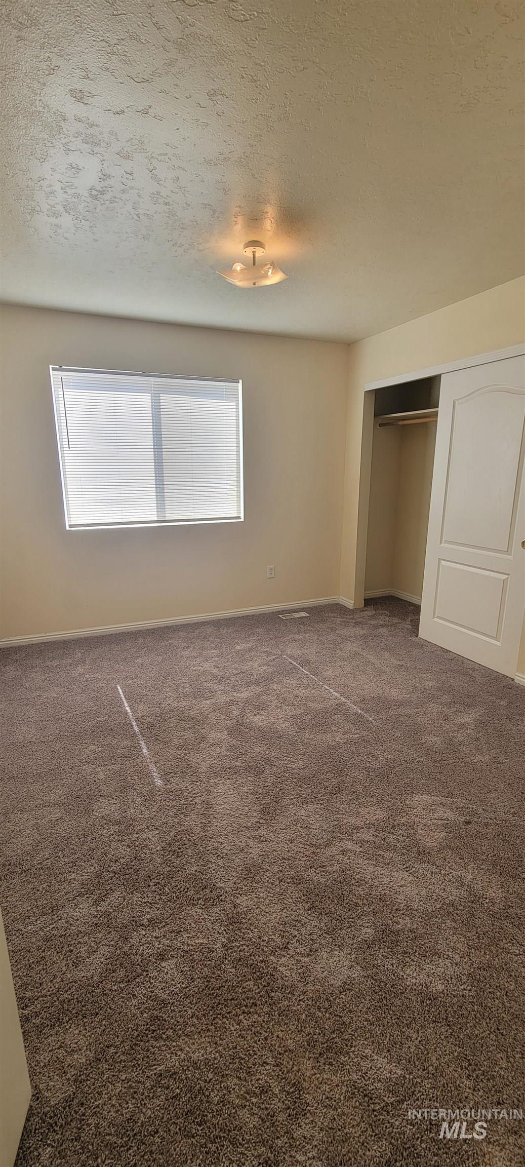 Unfurnished bedroom featuring a textured ceiling, carpet, and a closet
