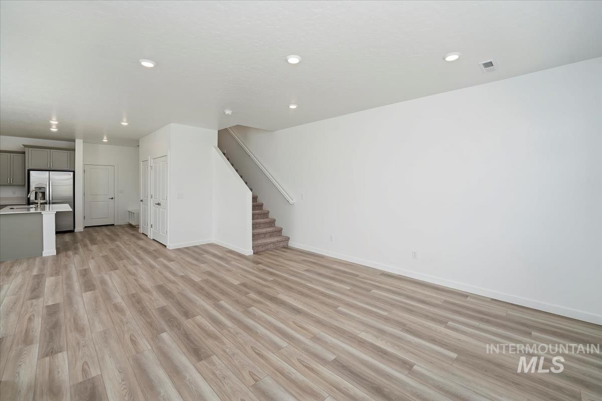 Unfurnished living room with stairway, light wood-style flooring, and recessed lighting