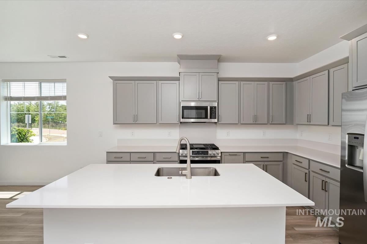 Kitchen featuring gray cabinets, appliances with stainless steel finishes, light countertops, wood finished floors, and recessed lighting