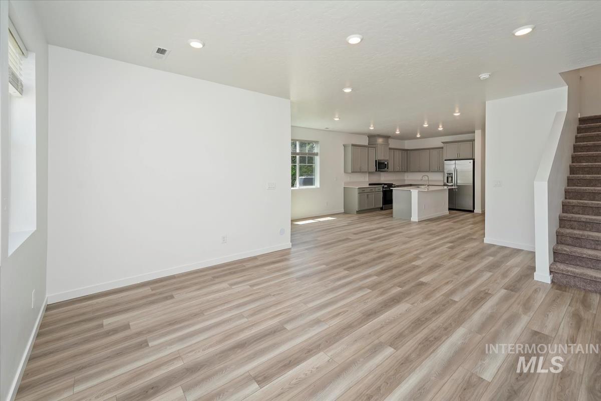 Unfurnished living room featuring stairway, light wood-style floors, and recessed lighting