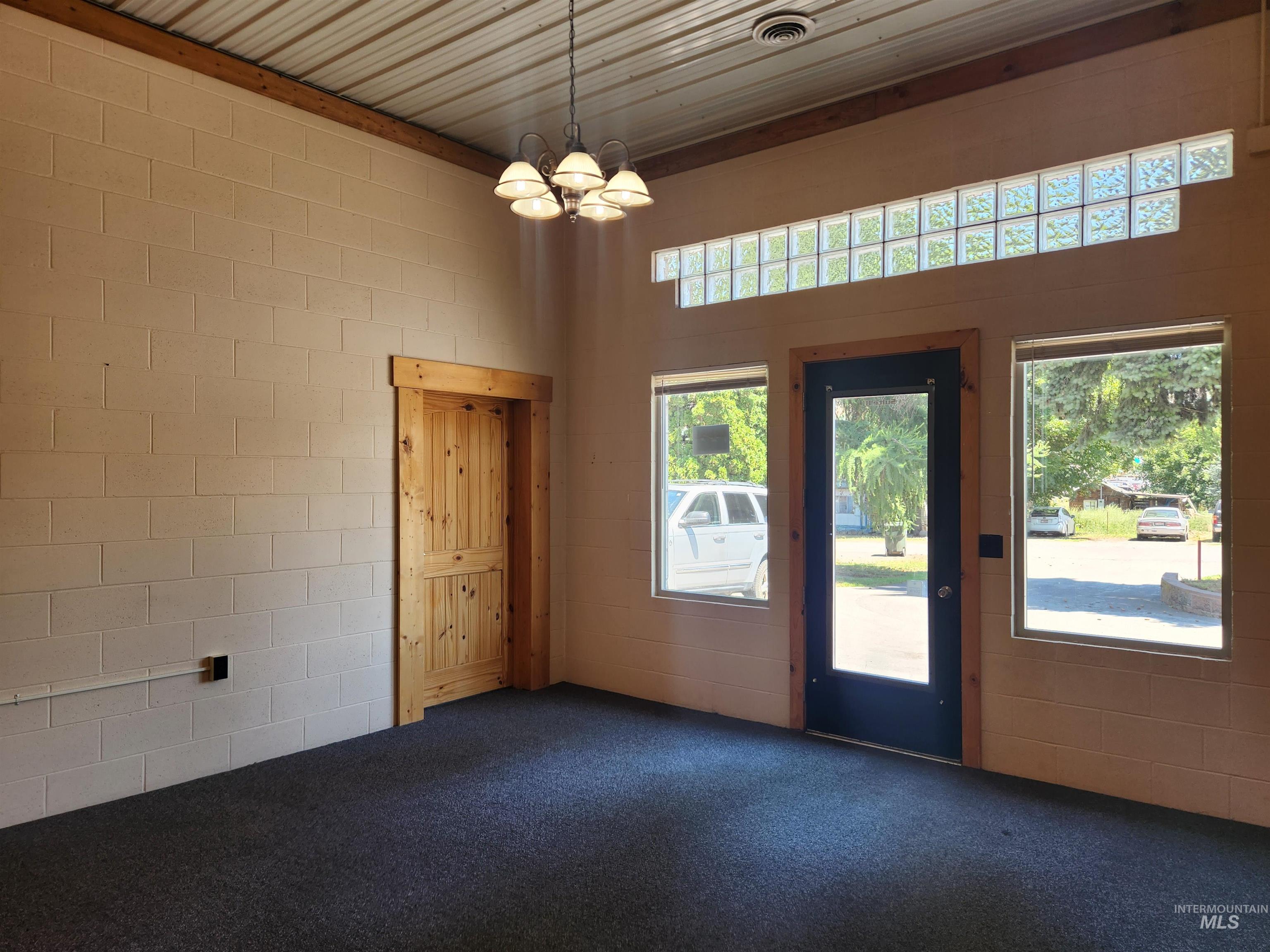 Empty room featuring dark carpet, a chandelier, and concrete block wall