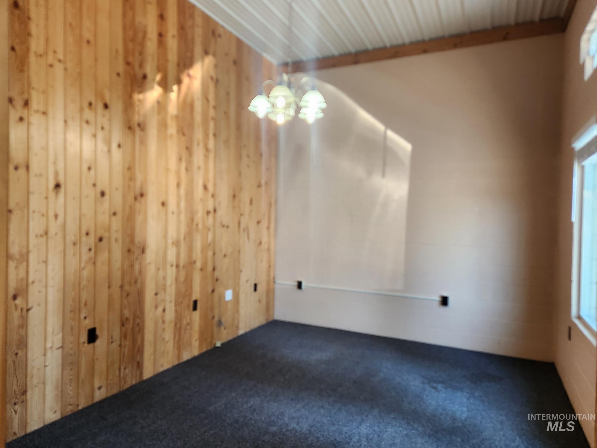 Unfurnished room featuring dark colored carpet and wooden walls