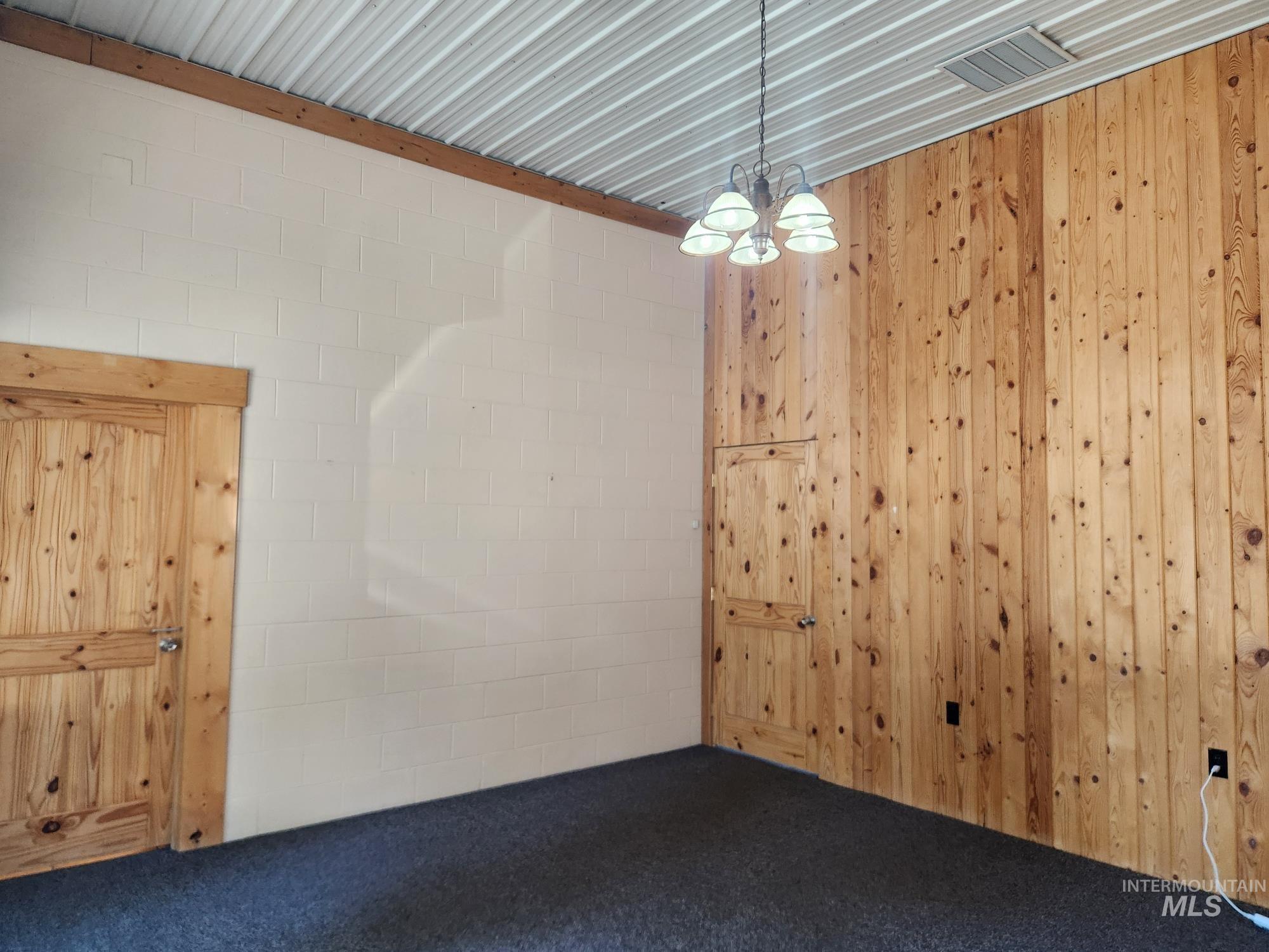 Carpeted empty room with a chandelier and wooden walls