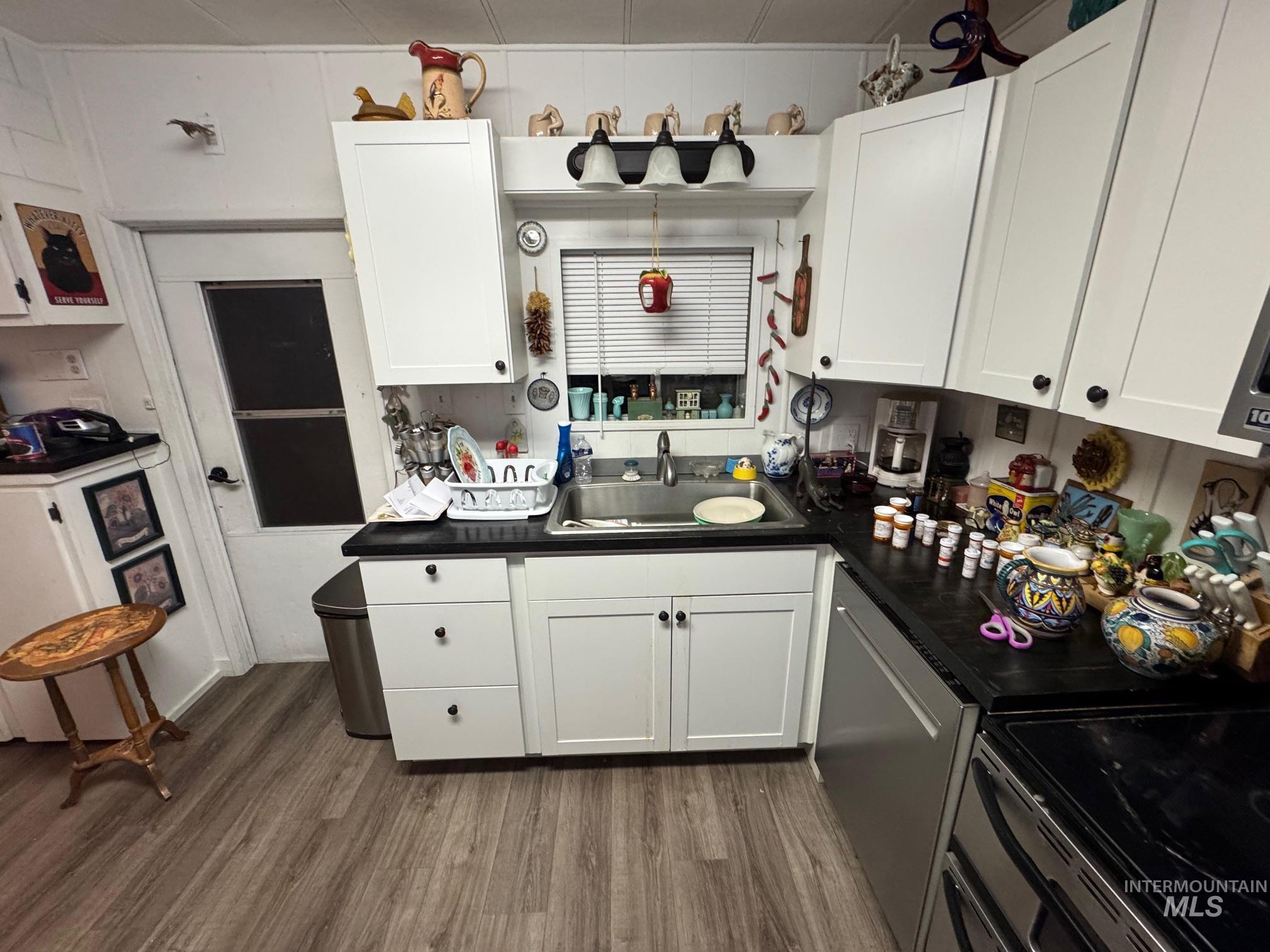 Kitchen with dark countertops, wood finished floors, white cabinets, stainless steel appliances, and washer and clothes dryer
