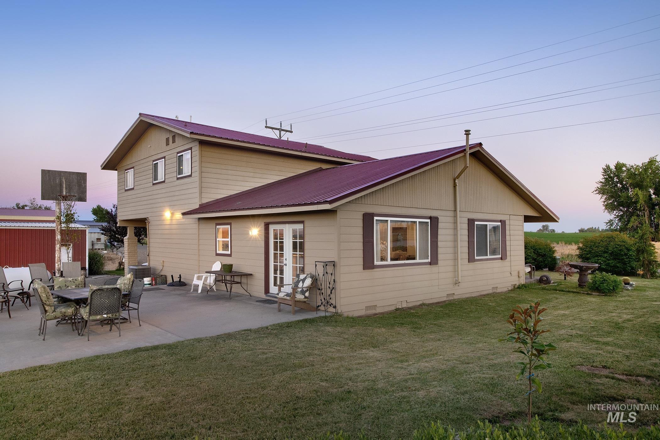 Back of house at dusk featuring a metal roof, a lawn, and a patio area