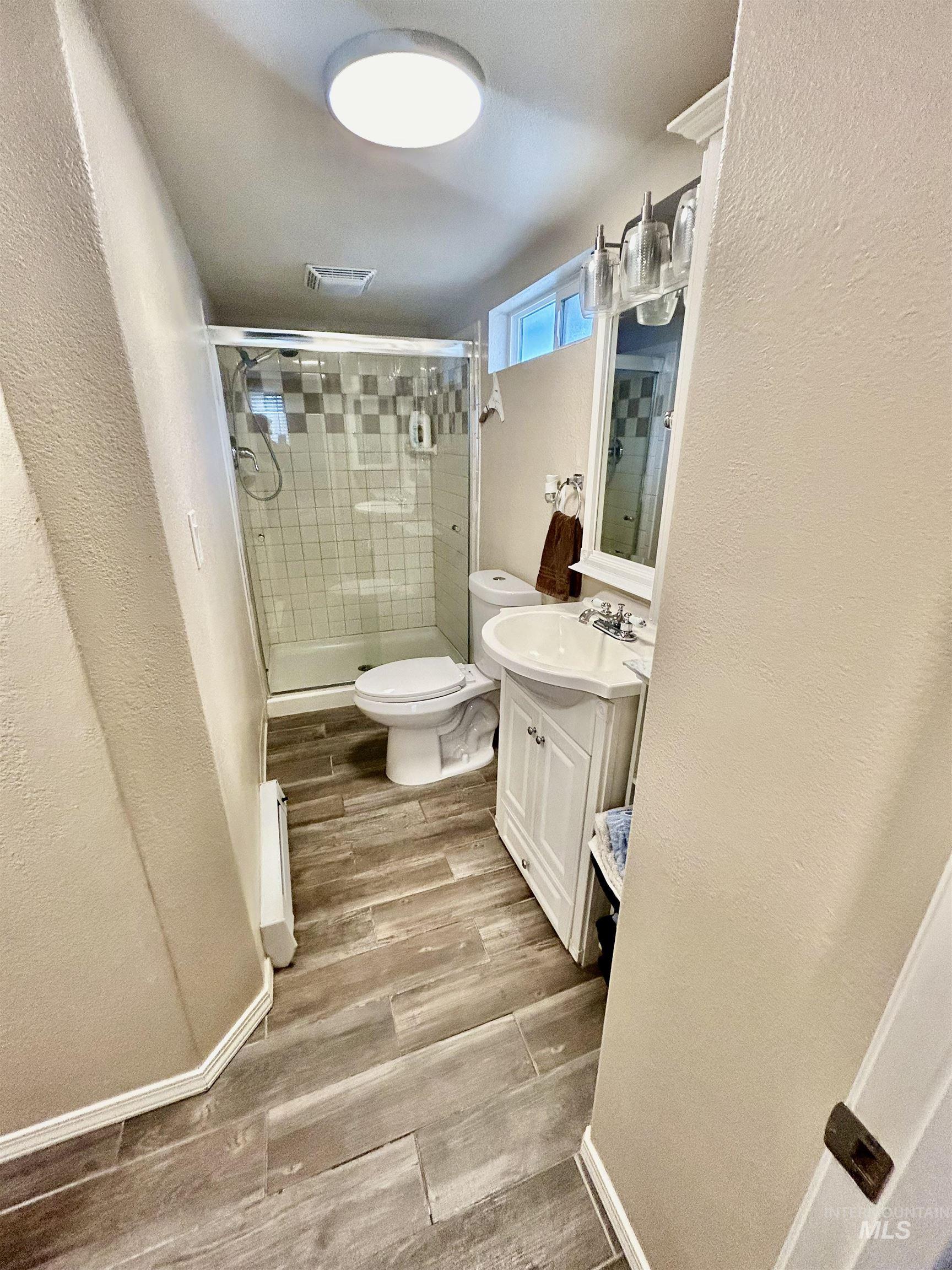 Bathroom featuring vanity, a stall shower, wood finished floors, a textured wall, and a baseboard radiator