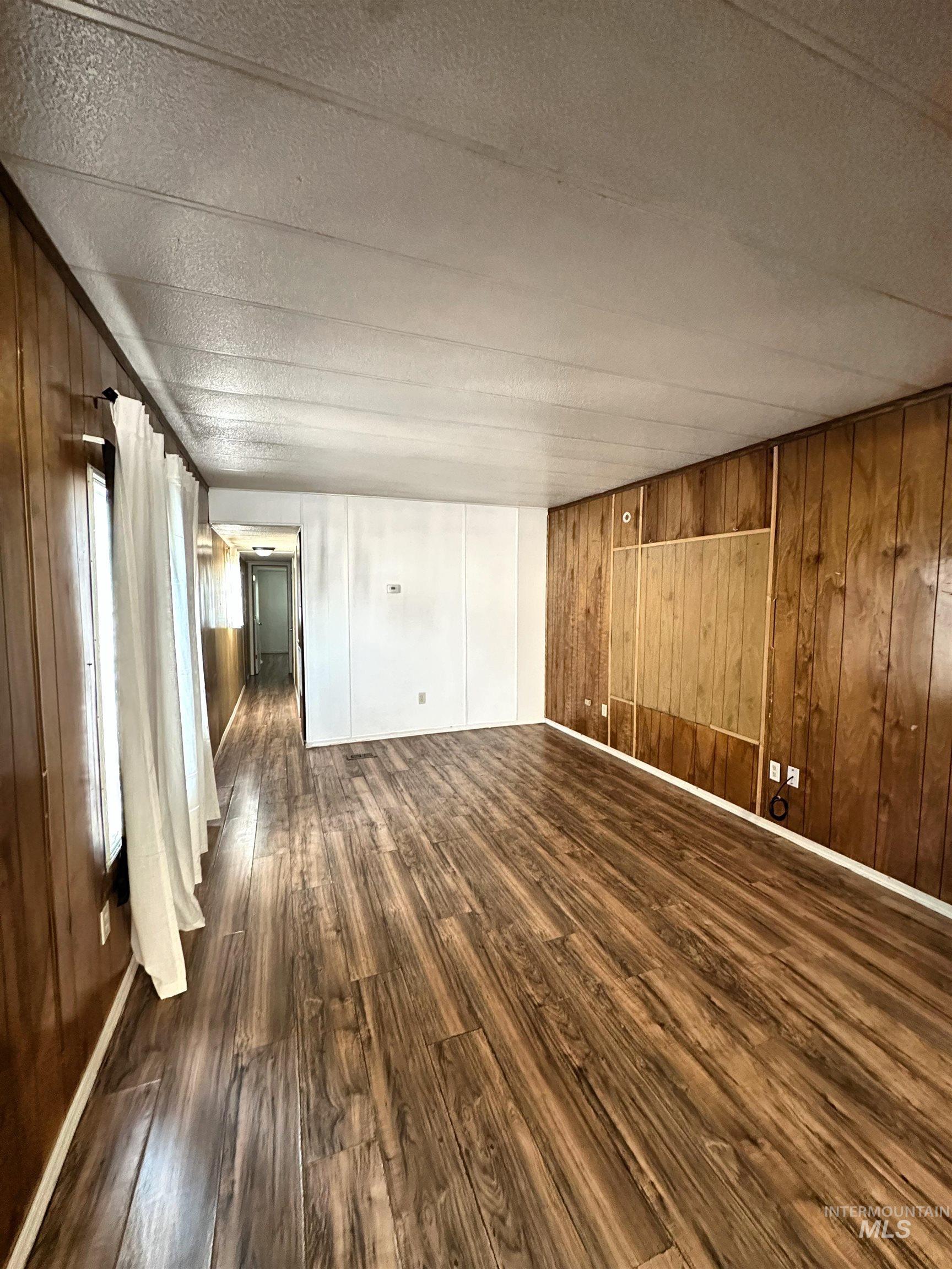Unfurnished living room featuring wooden walls, dark wood-type flooring, and a textured ceiling