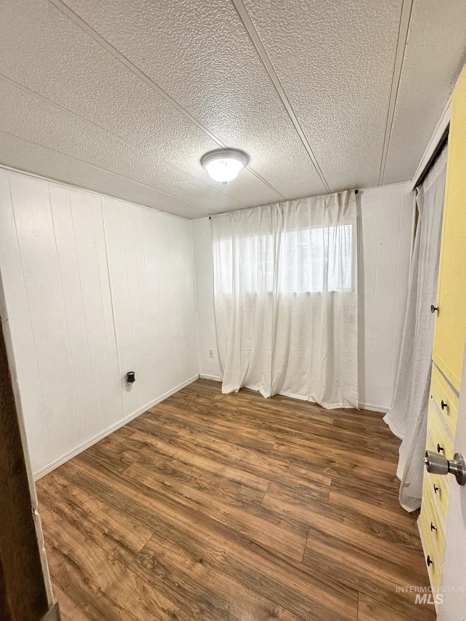 Spare room with wood finished floors, a textured ceiling, and wooden walls