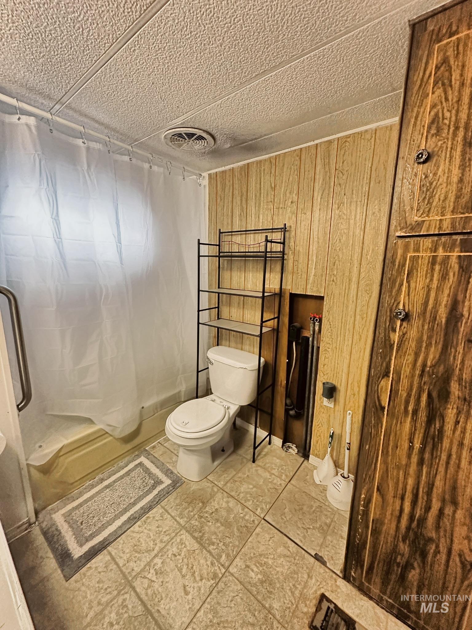 Full bath featuring wooden walls, a textured ceiling, and shower / tub combo with curtain