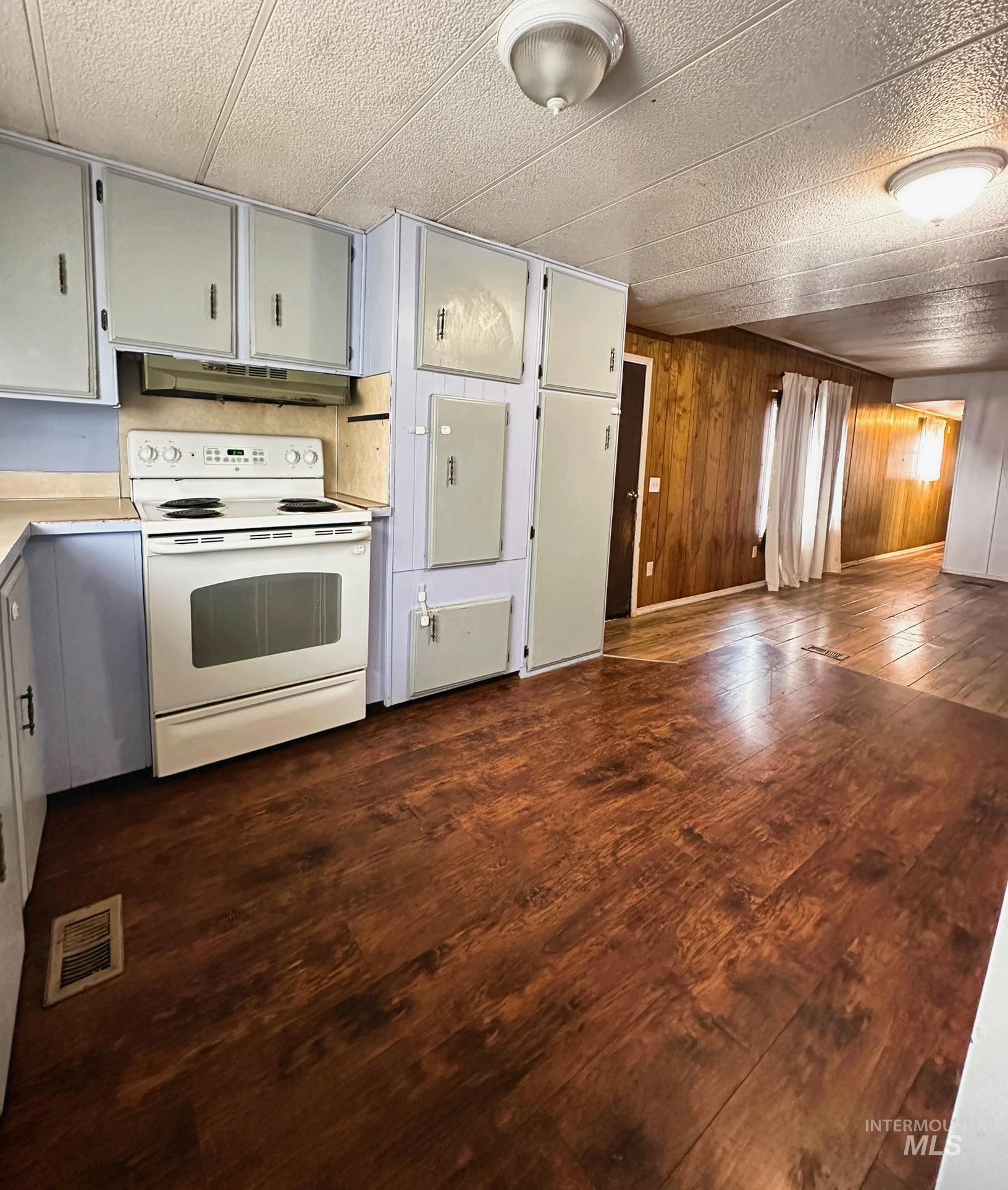 Kitchen with electric stove, light countertops, under cabinet range hood, gray cabinets, and dark wood-type flooring