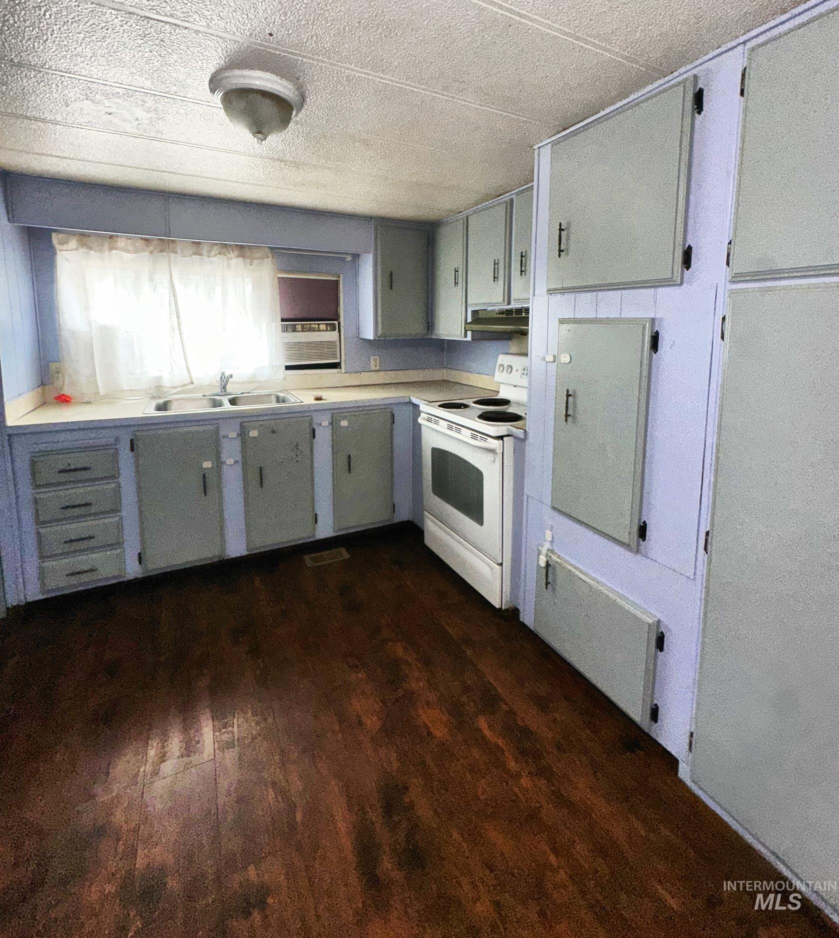 Kitchen featuring white range with electric stovetop, dark wood finished floors, light countertops, gray cabinets, and under cabinet range hood
