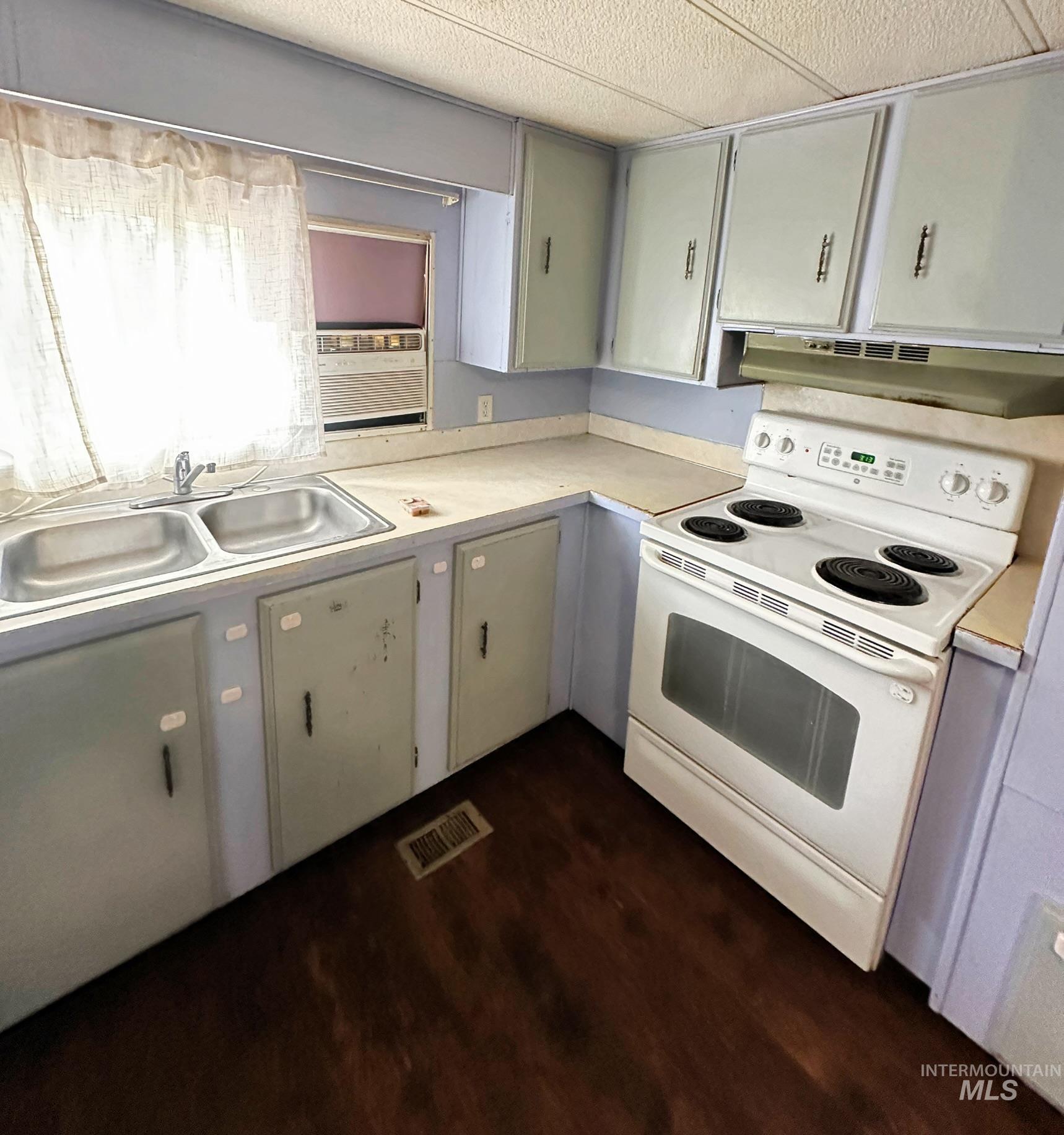 Kitchen with white range with electric stovetop, under cabinet range hood, light countertops, and dark wood-style flooring