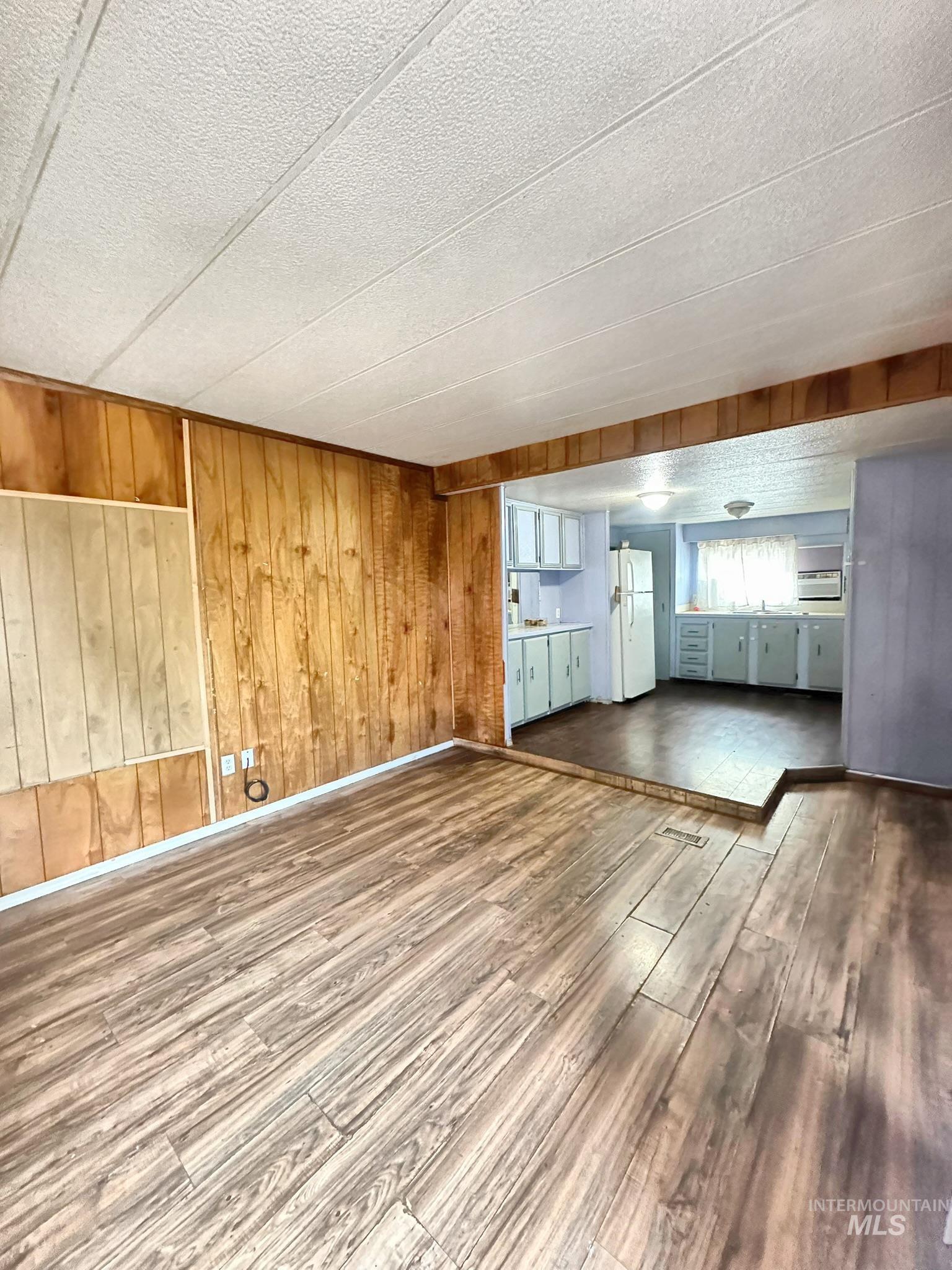 Unfurnished living room with wood finished floors, wood walls, and a textured ceiling