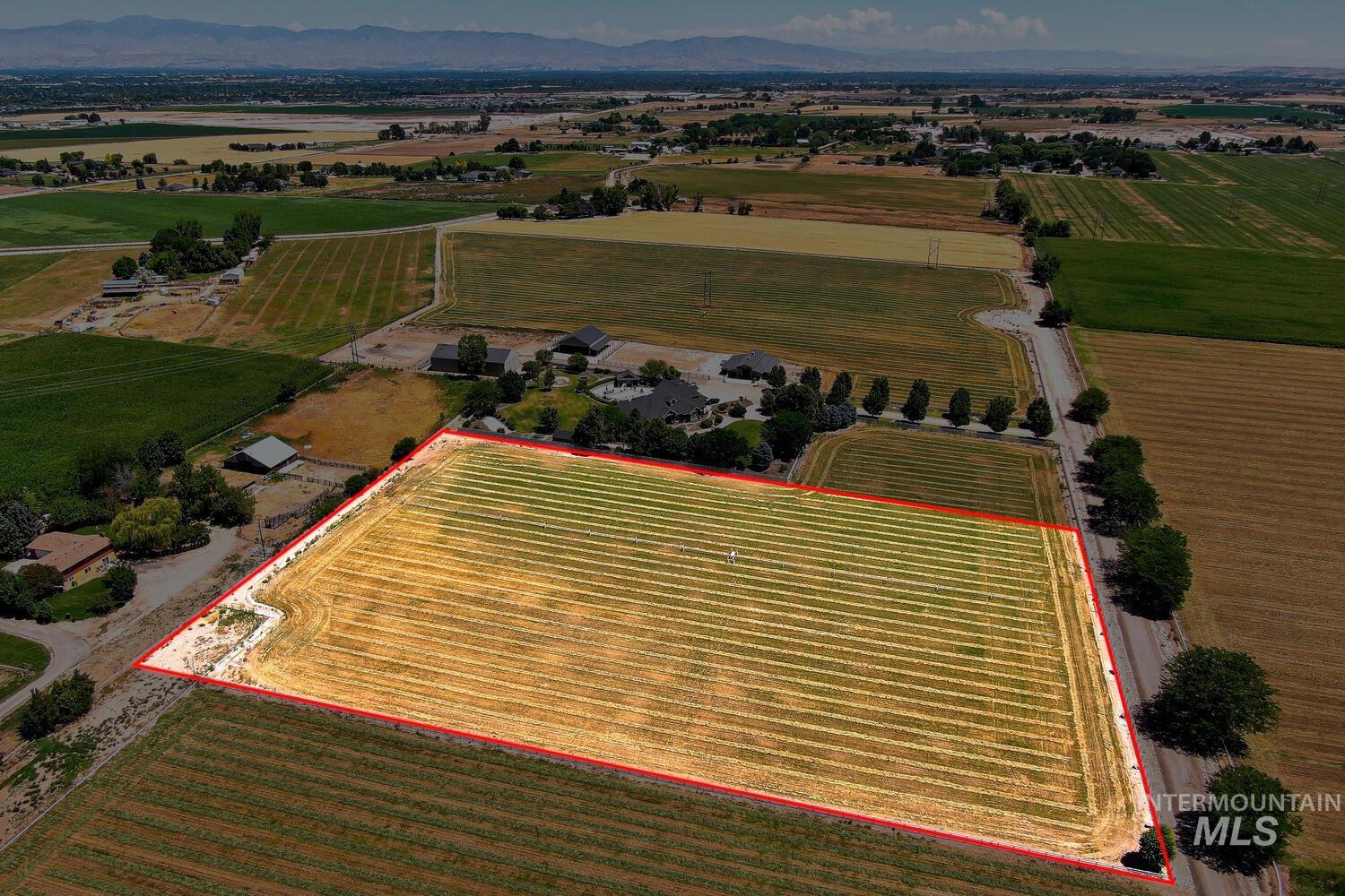Aerial view of sparsely populated area with farmland, property parcel outlined, and mountains