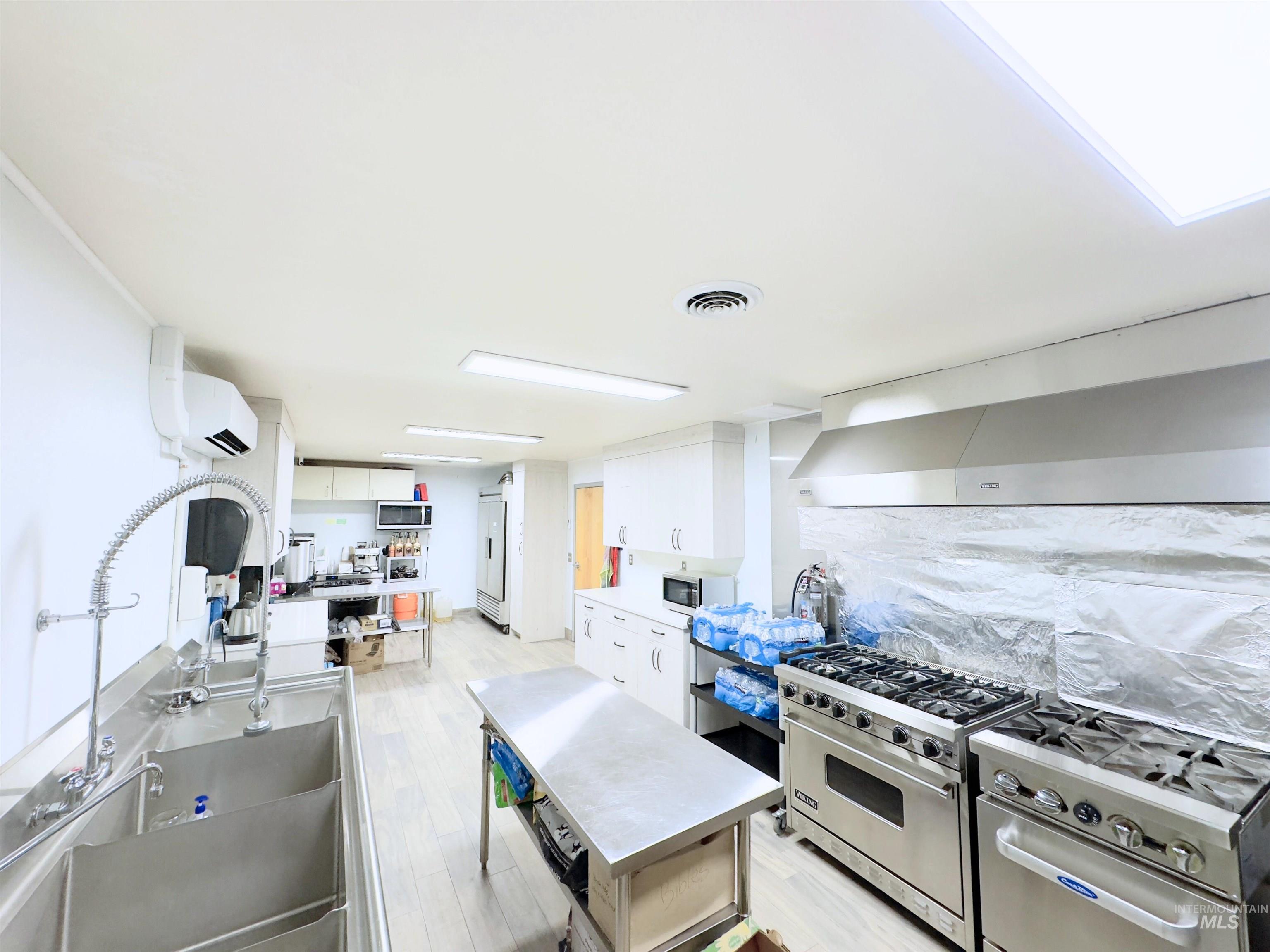 Kitchen featuring high quality appliances, white cabinetry, light wood-type flooring, and decorative backsplash