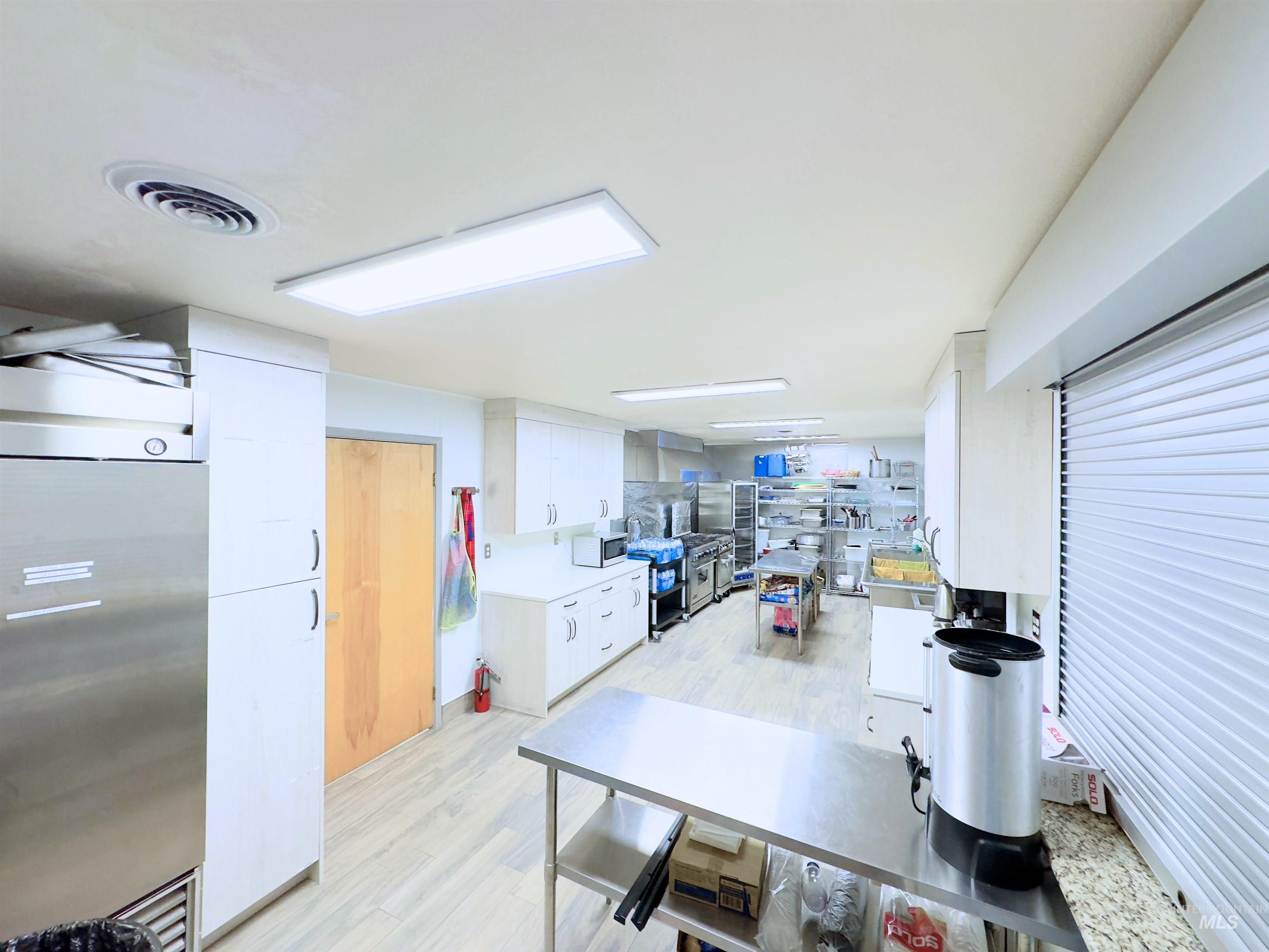 Kitchen with stainless steel fridge, white cabinets, light wood-style flooring, and white microwave