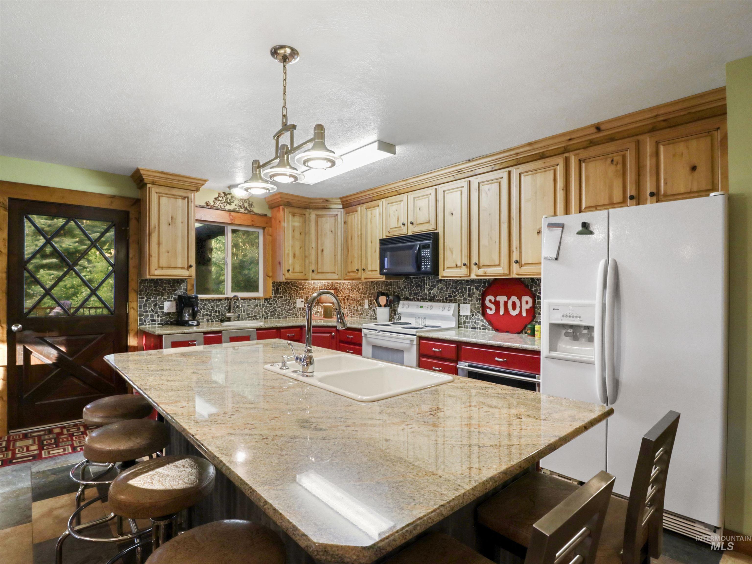 Kitchen with white appliances, tasteful backsplash, a kitchen island with sink, and a breakfast bar area